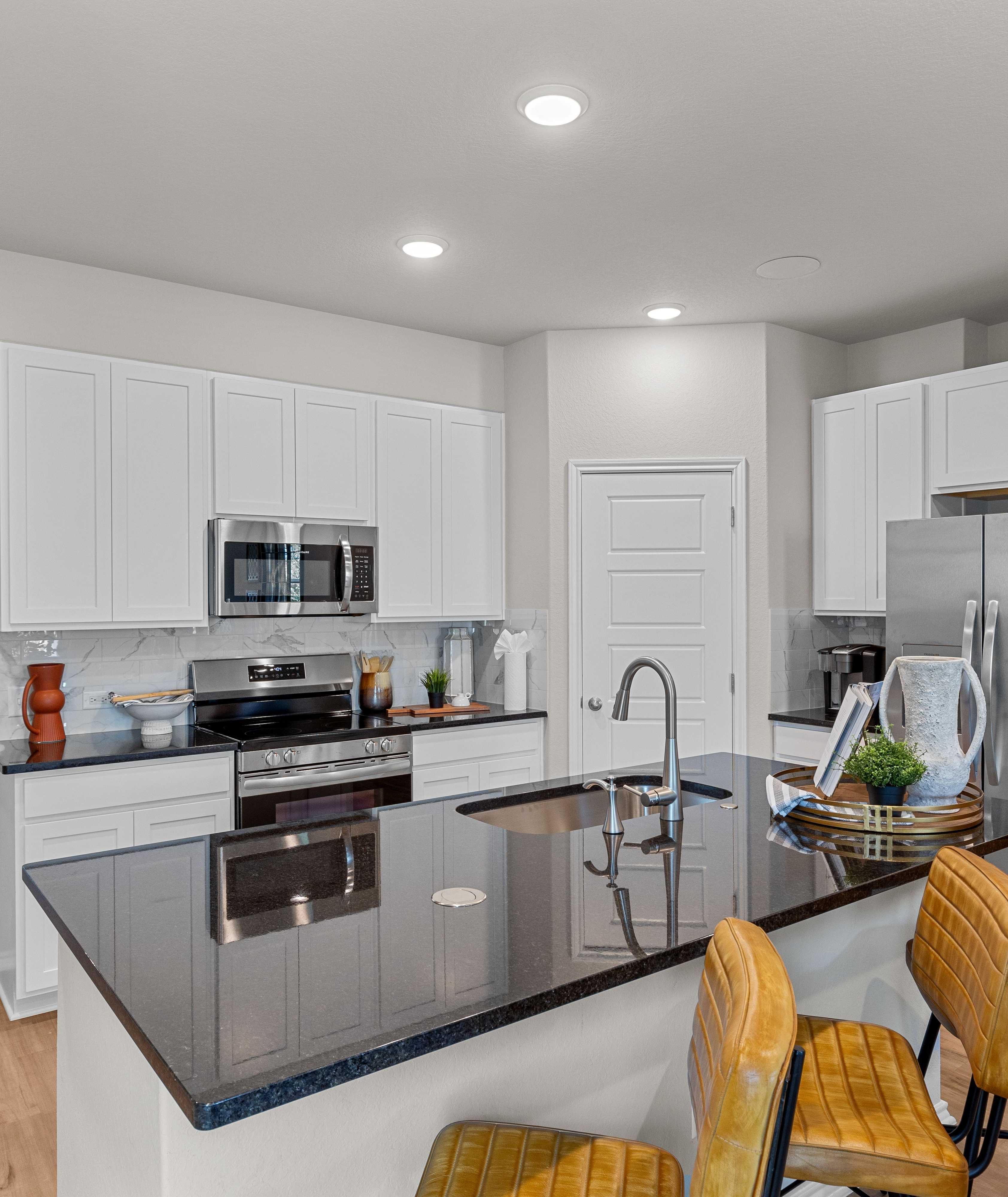 Spacious modern kitchen at Meadows at Oak Creek in San Antonio TX featuring white cabinets, black granite island, stainless steel appliances, and hardwood floors