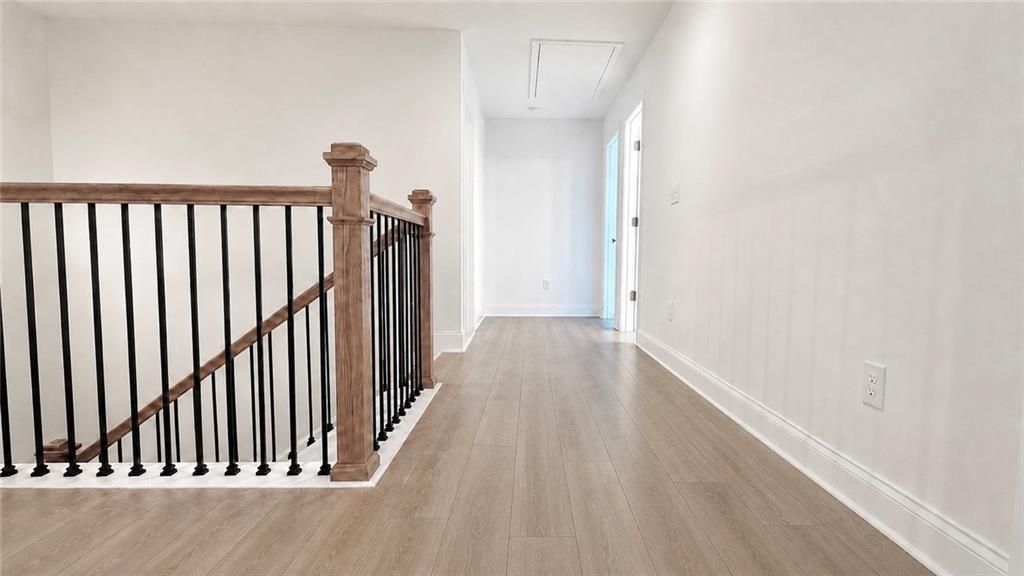 Bright second-floor landing with wood railing and LVP flooring in The Hickory C plan at Wehunt Meadows, Hoschton, GA.