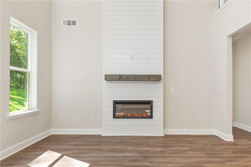 Shiplap fireplace with gas flames and wood mantel in open family room, large window overlooking greenery, Danbury E home in Buford, Georgia