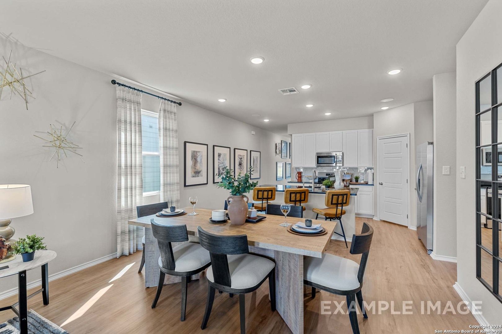 Elegant open-concept dining area with modern wooden table, upholstered chairs, and adjacent white kitchen in Davidson Homes The Sabine B, San Antonio