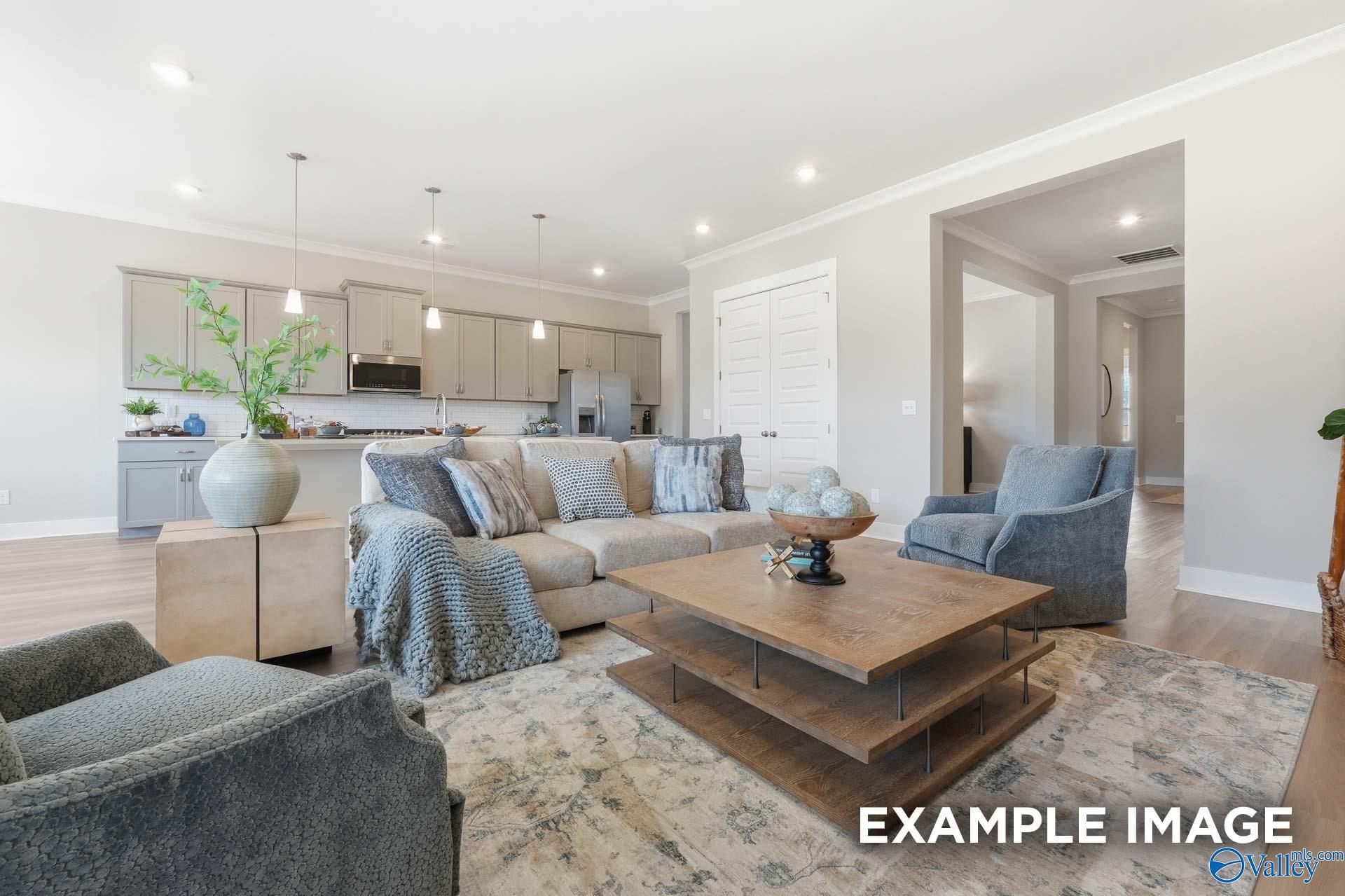 Cozy great room with gray sectional sofa, armchairs, and open kitchen in Evermore Homes The Oxford B, Owens Cross Roads, AL