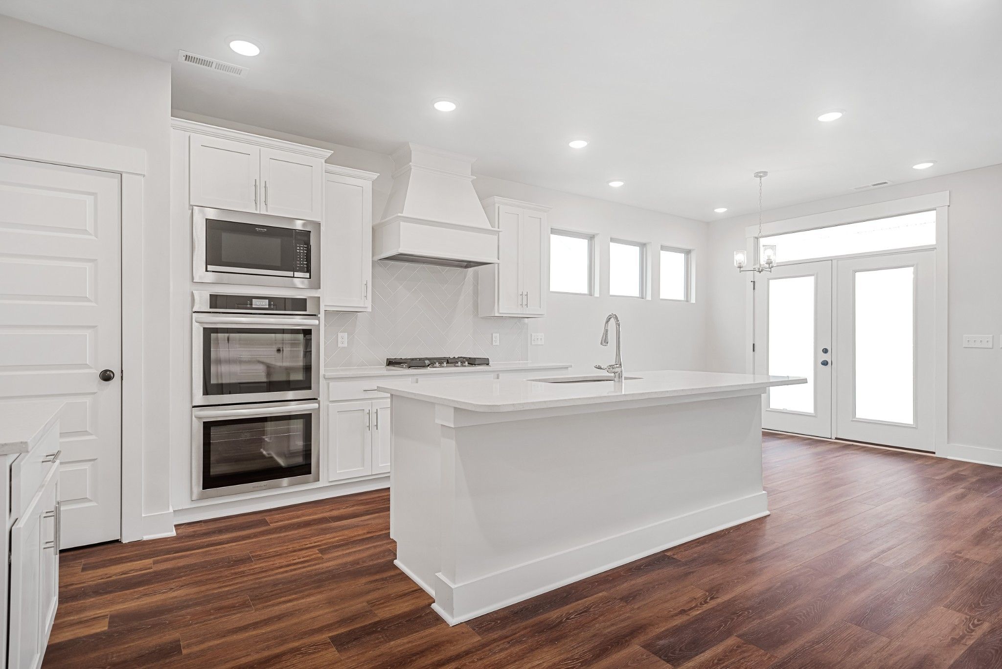 Modern white kitchen featuring quartz island, double ovens, gas range, and subway tile backsplash in Davidson Homes The Ash A, White House TN