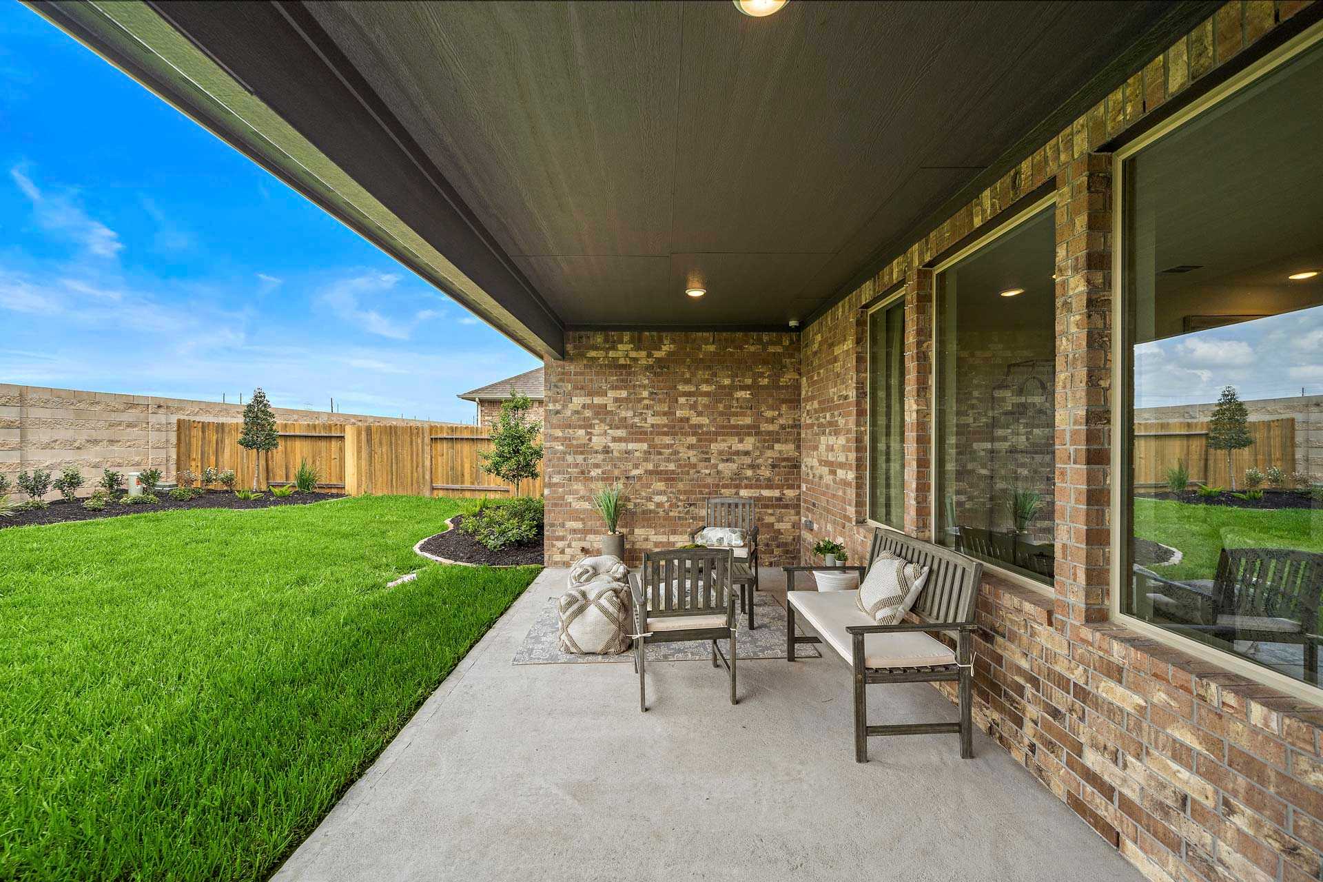 Spacious covered patio with brick walls, large windows, outdoor seating, and green lawn at Sierra Vista in Rosharon, Texas