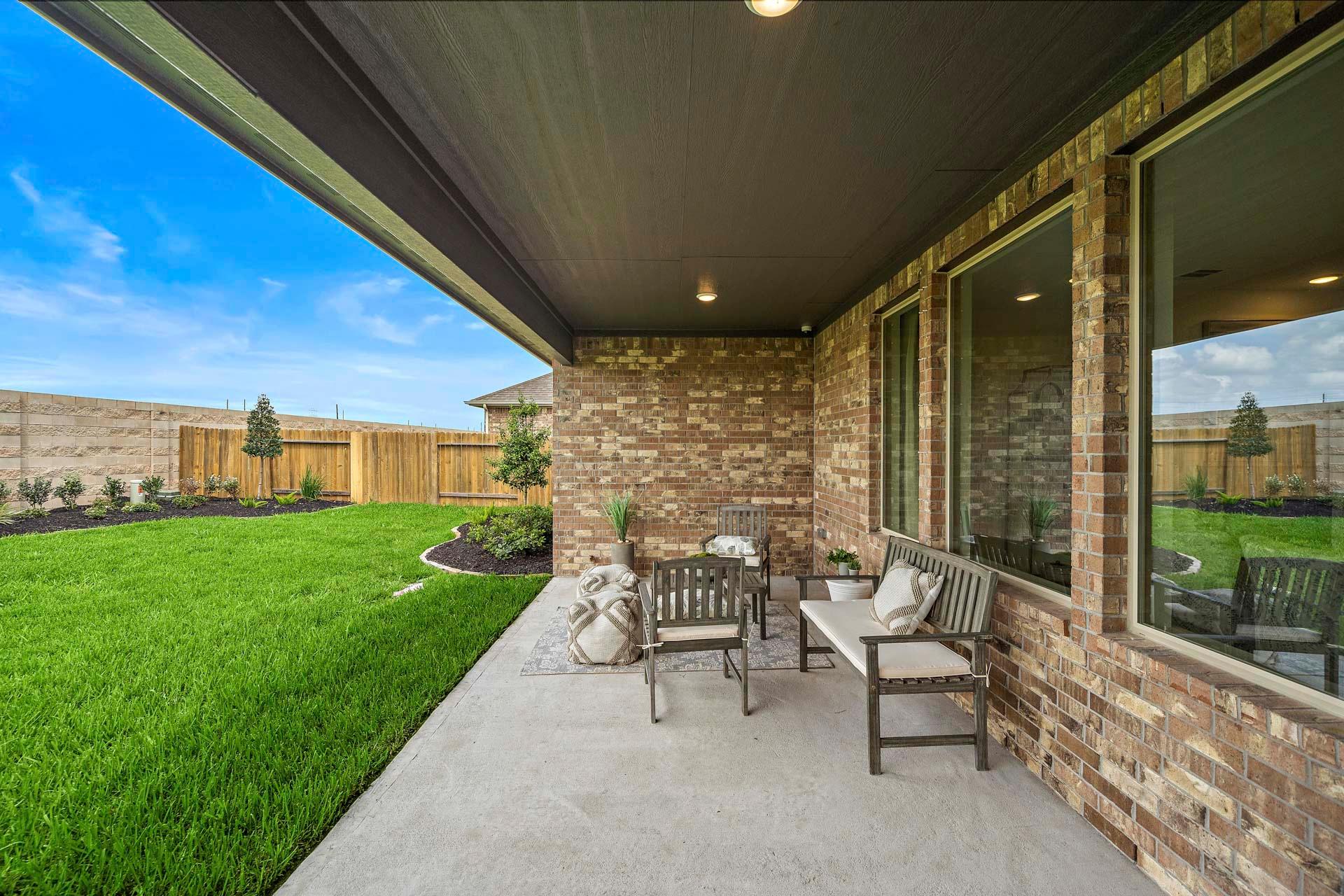 Spacious covered patio with brick walls, large windows, outdoor seating, and green lawn at Sierra Vista in Rosharon, Texas