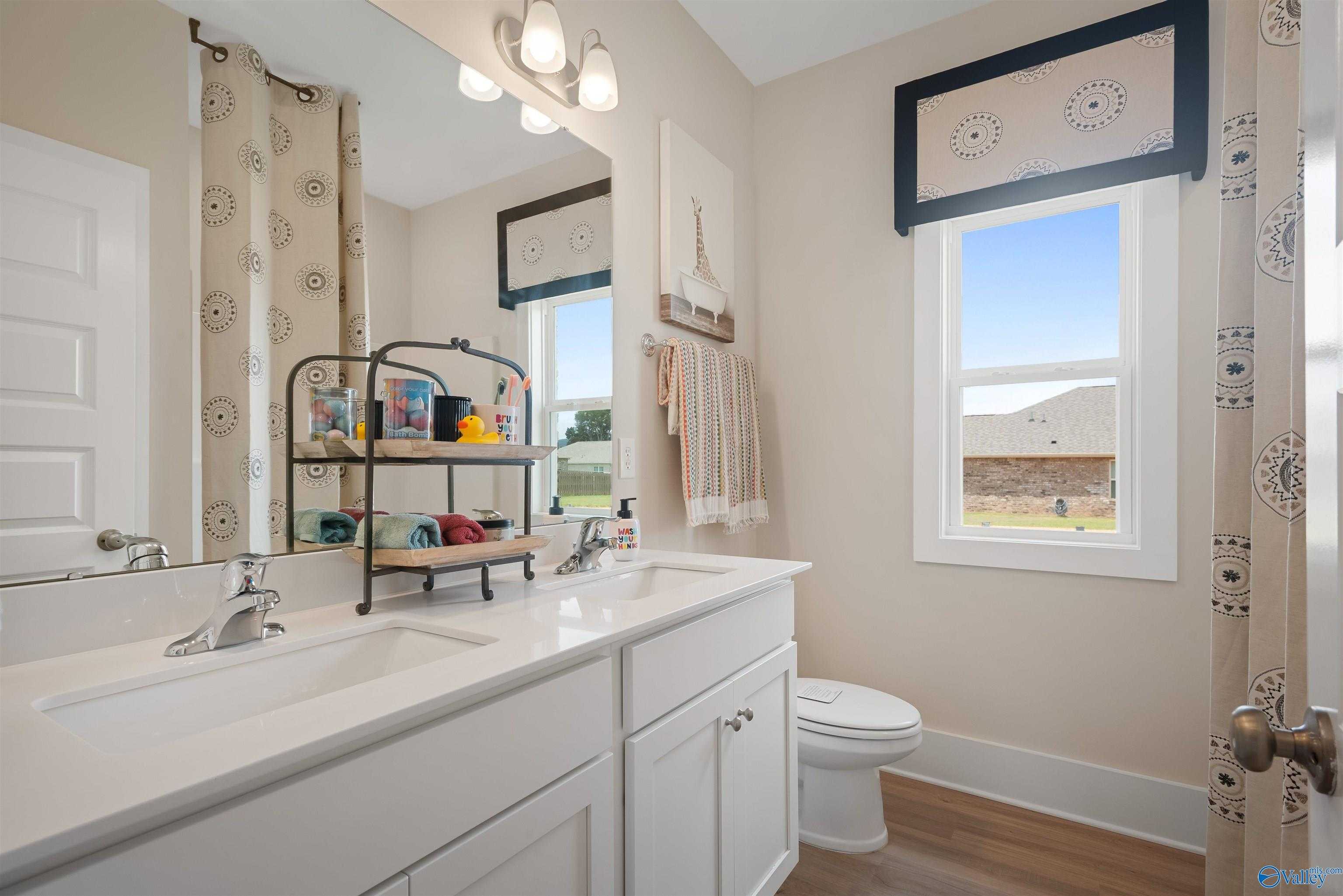 Modern guest bathroom with white double vanity, large mirror, Eiffel Tower art, and window view in Davidson Homes The Everett, New Market, Alabama