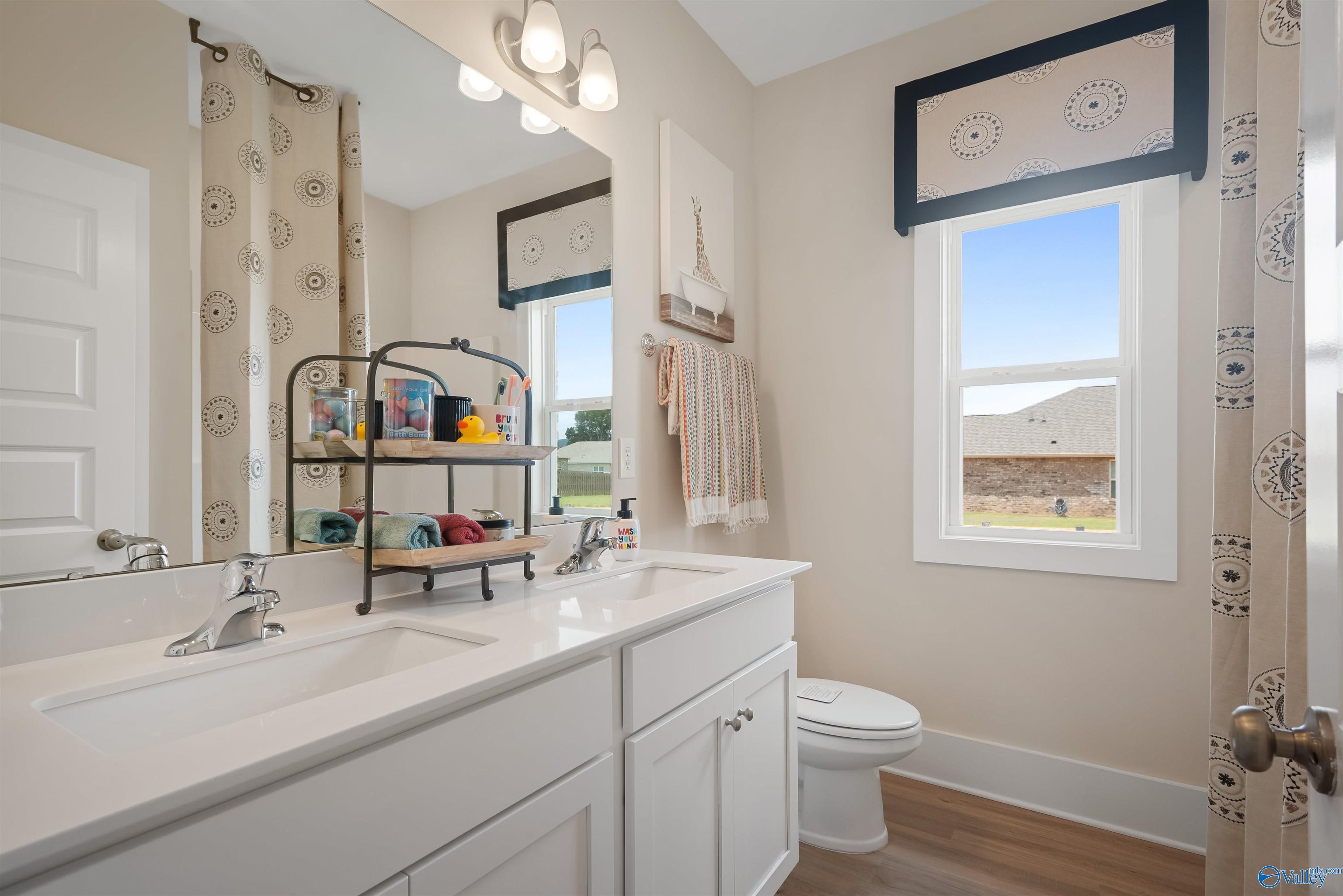 Modern guest bathroom with white double vanity, large mirror, Eiffel Tower art, and window view in Davidson Homes The Everett, New Market, Alabama
