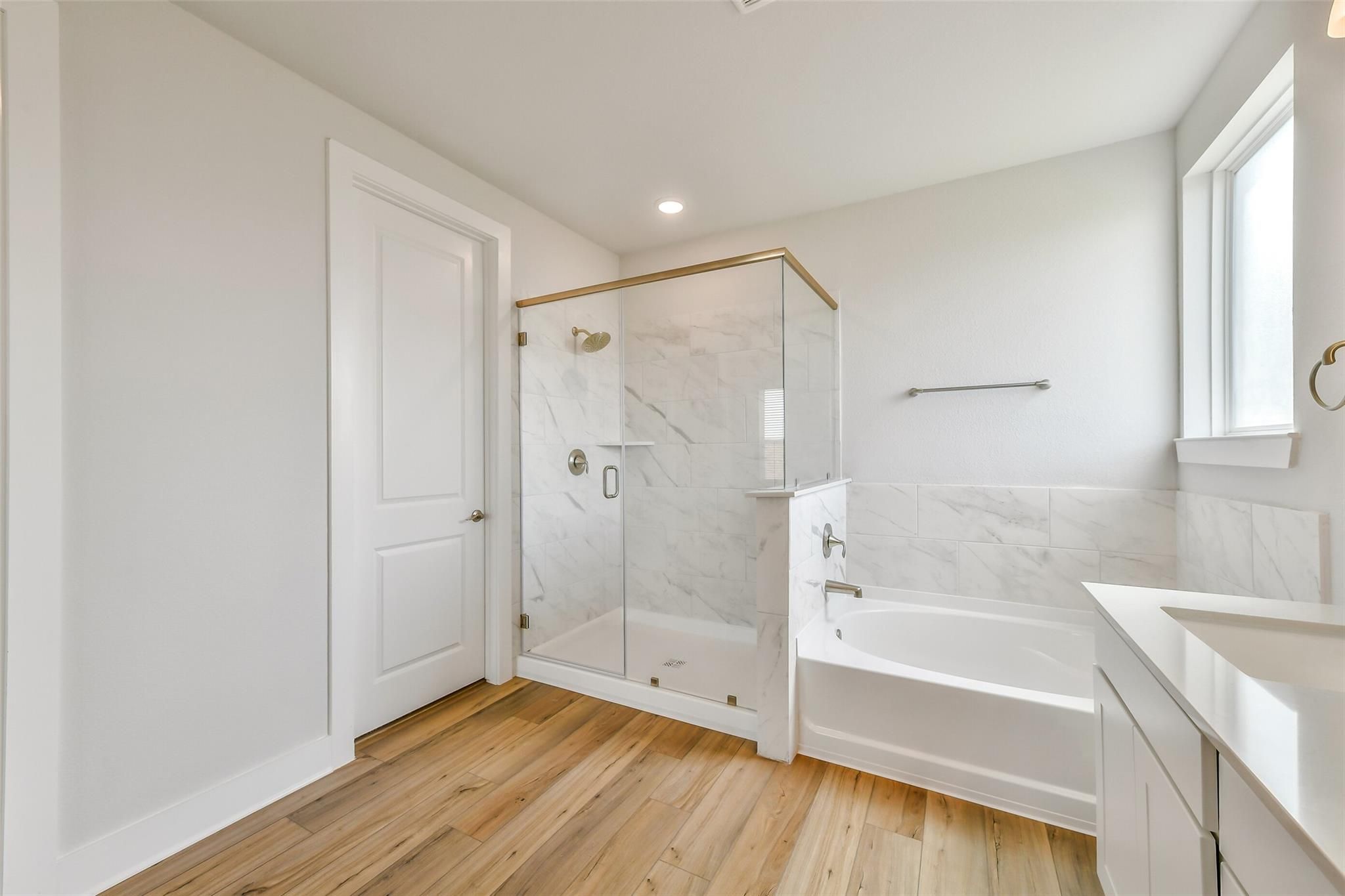 Elegant master bathroom with frameless glass marble shower, soaking tub, white vanity, hardwood floors in Davidson Homes The Victoria A, Lago Mar