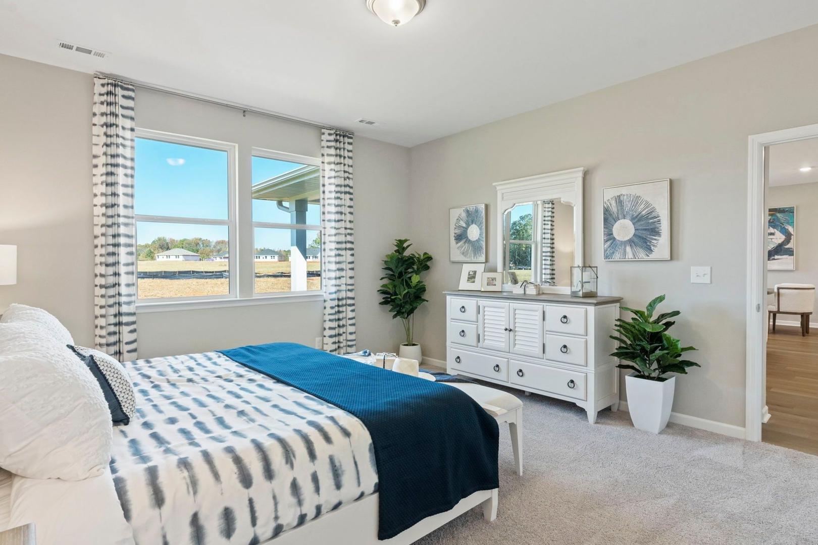 Spacious master bedroom in The Phoenix A featuring king bed, white dresser, potted plants, and large windows