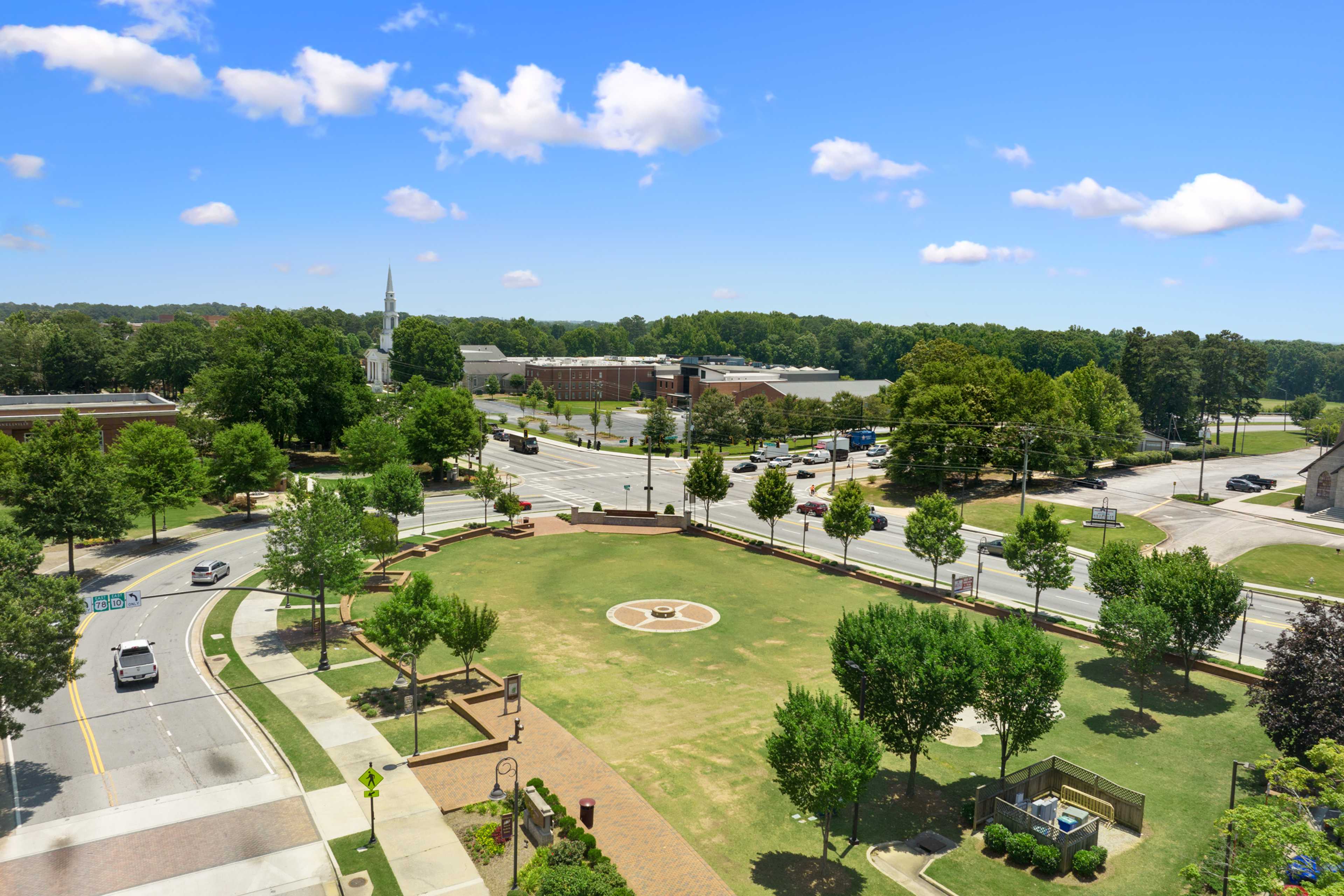 Aerial view of Kelly Preserve park in Loganville Georgia featuring central grassy meadow trees pathways and nearby church steeple