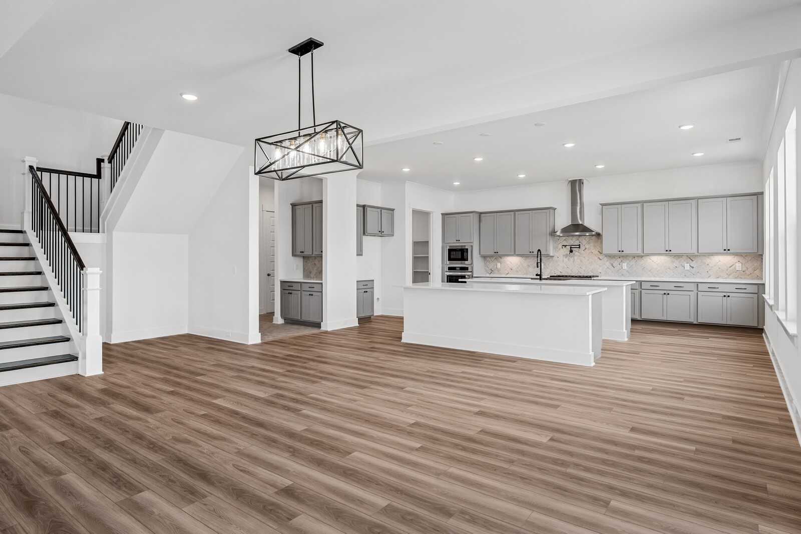 Expansive open-concept kitchen with white cabinets, large island, hardwood floors, and staircase in Davidson Homes The Alston A, Murfreesboro, TN