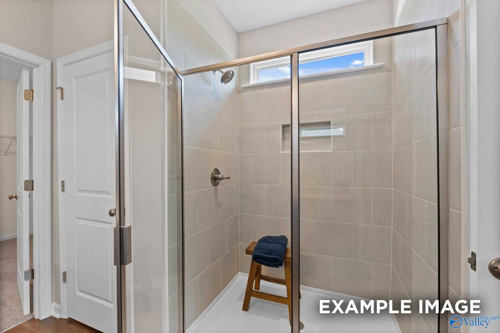 Modern walk-in shower with frameless glass enclosure, tiled surround, and bench in master bath of Evermore Homes The Arcadia M, Owens Cross Roads, Alabama