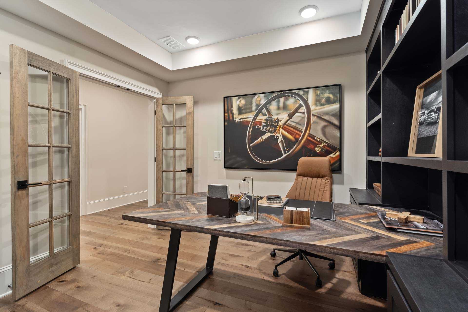 Modern home office at Tanglewood in East Cobb GA by Davidson Homes with chevron desk, leather chair, bookshelves, and car wheel art