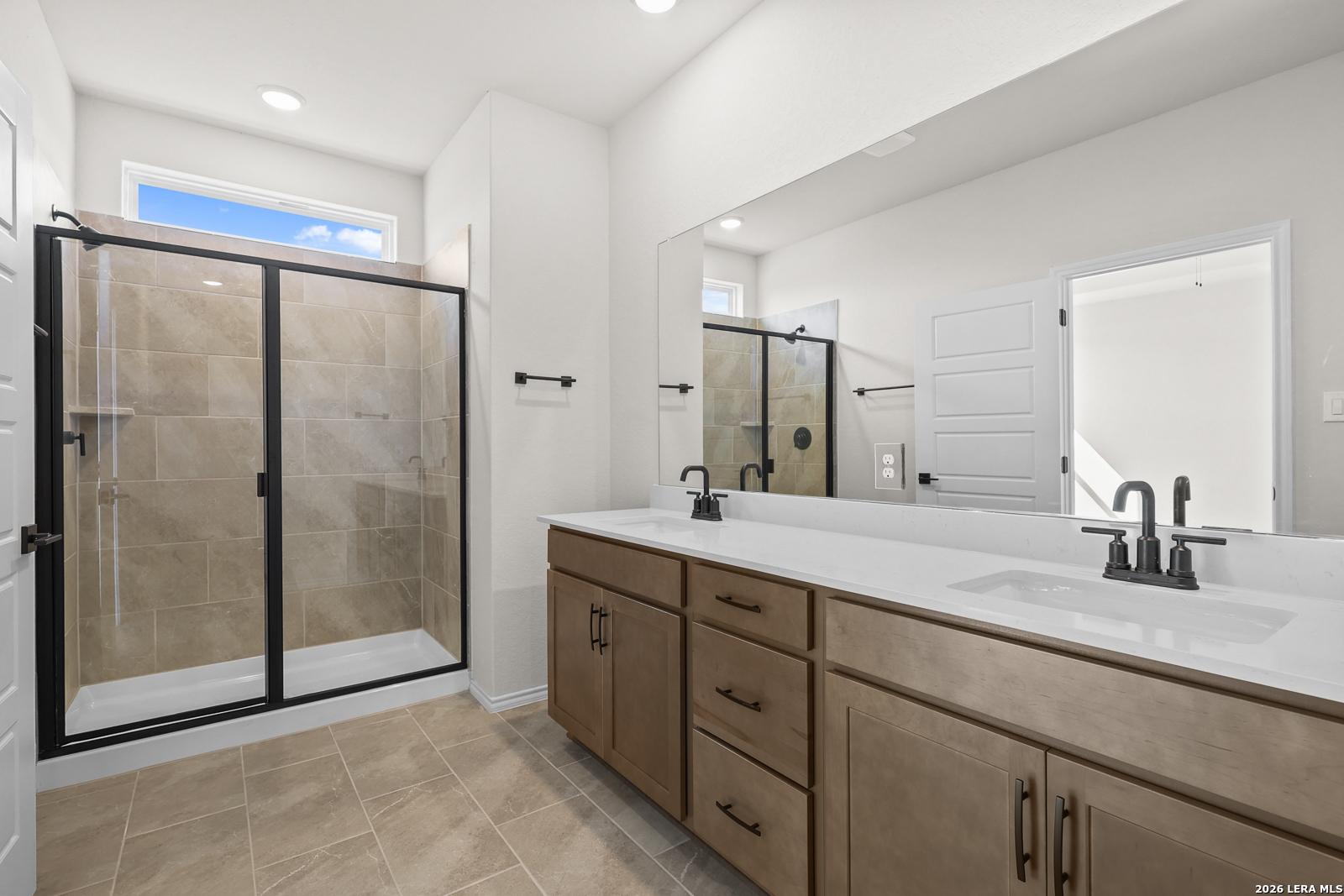 Modern master bathroom with double vanity, walk-in tile shower, and matte black fixtures in Davidson Homes Glenwood E, San Antonio
