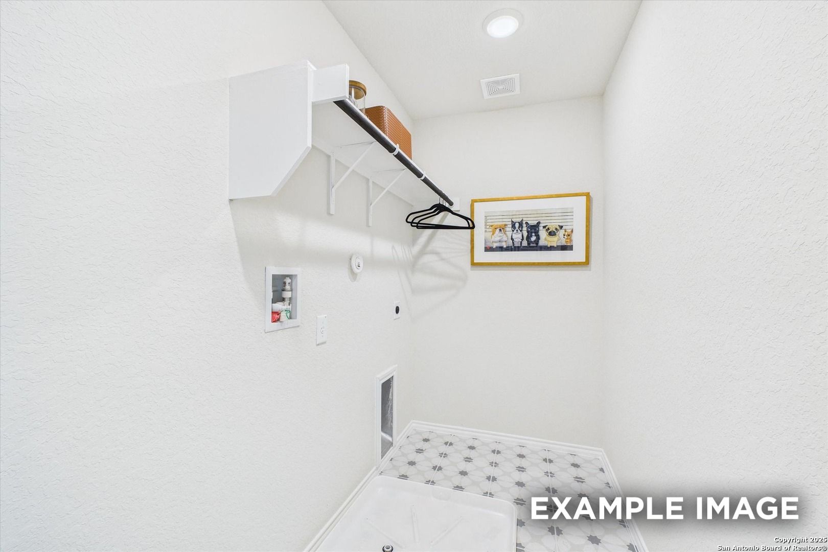 Bright white laundry room with built-in shelves, wooden hanging rod, framed art, and patterned tile floor in Davidson Homes The Florence C, San Antonio
