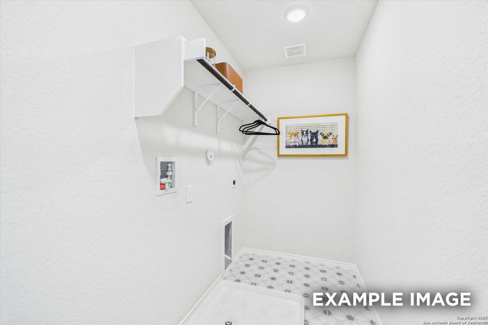 Bright white laundry room with built-in shelves, wooden hanging rod, framed art, and patterned tile floor in Davidson Homes The Florence C, San Antonio
