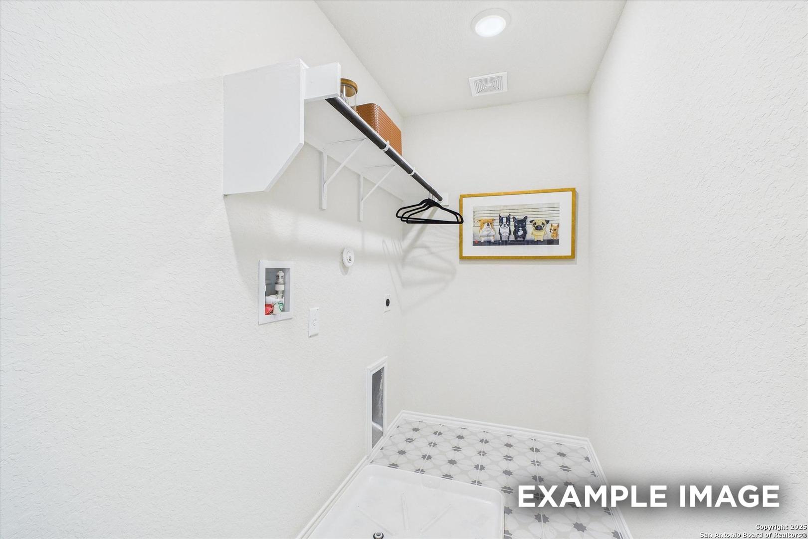 Bright white laundry room with built-in shelves, wooden hanging rod, framed art, and patterned tile floor in Davidson Homes The Florence C, San Antonio