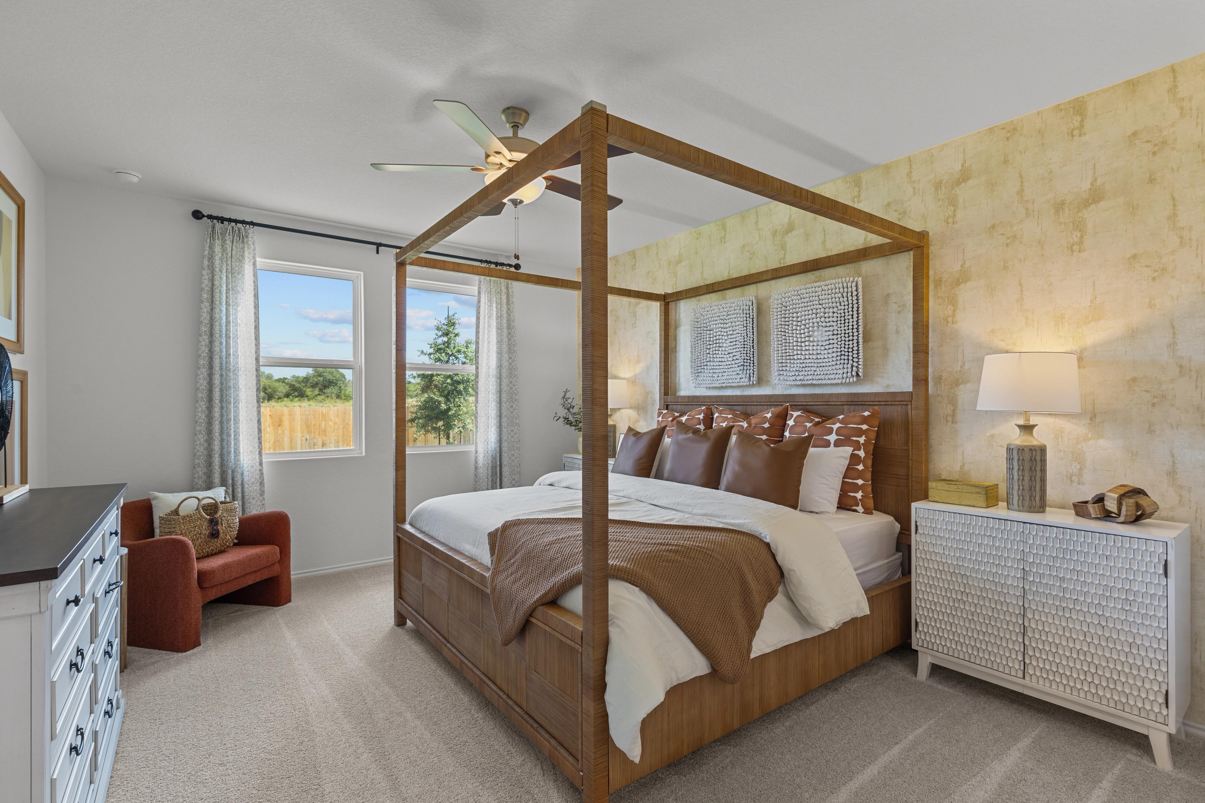 Spacious master bedroom in The Daphne G with wooden canopy bed, ceiling fan, neutral decor and large windows