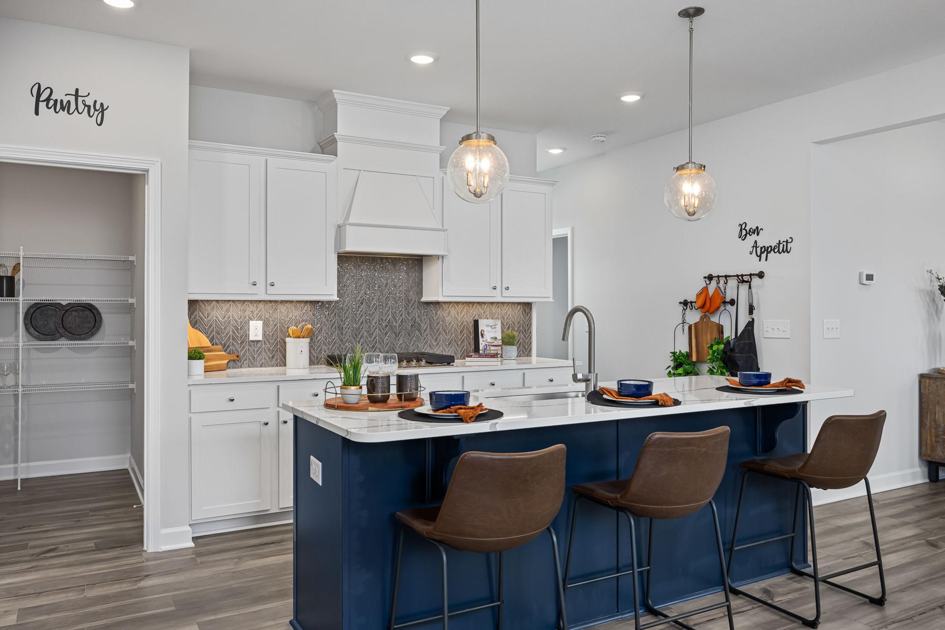 Spacious modern kitchen in Beverly Place, Four Oaks NC with white shaker cabinets, navy island, pendant lights, and pantry