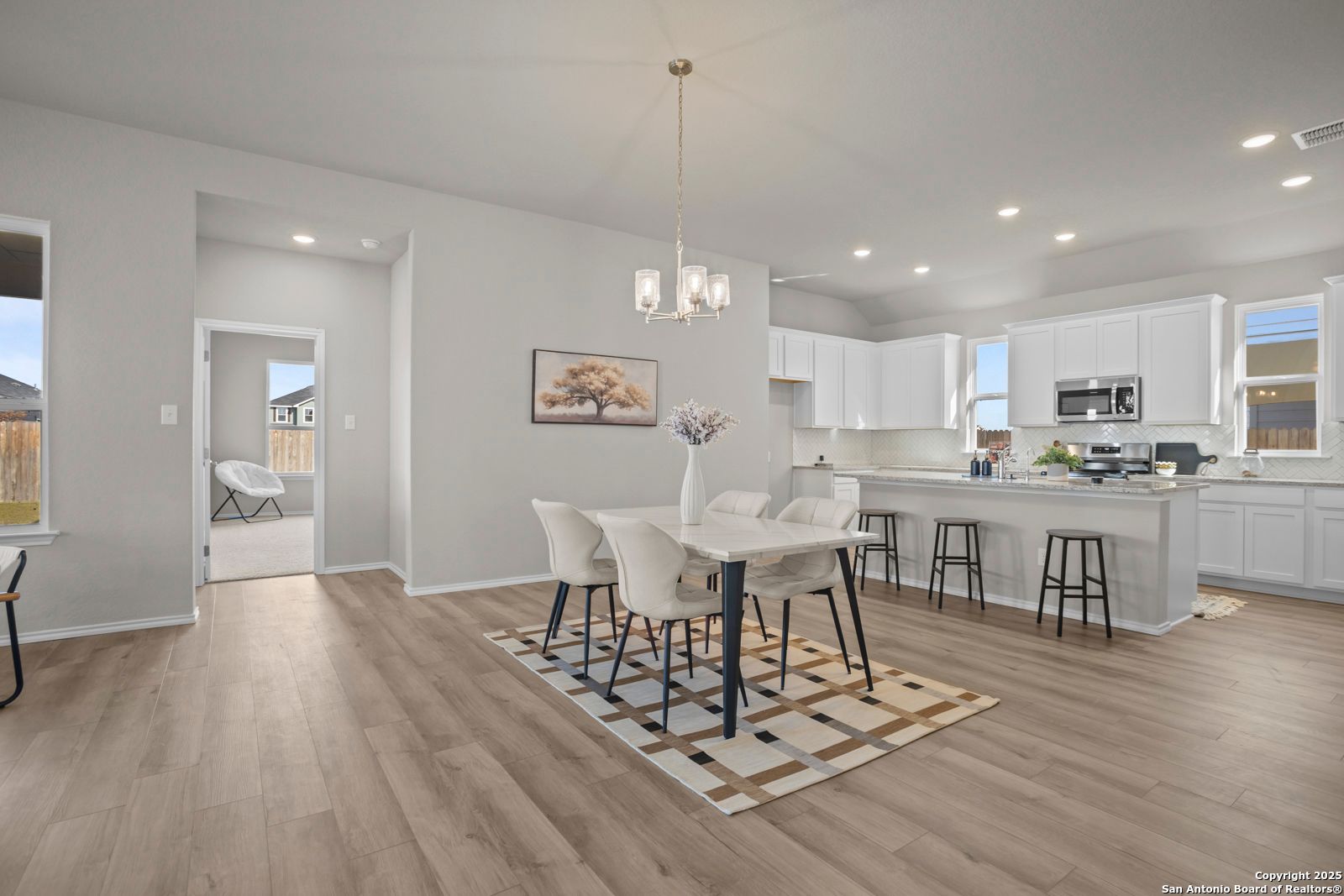 Open-concept dining area with white table, chairs, and patterned rug beside white cabinet kitchen in Davidson Homes The Collin B, Seguin, Texas