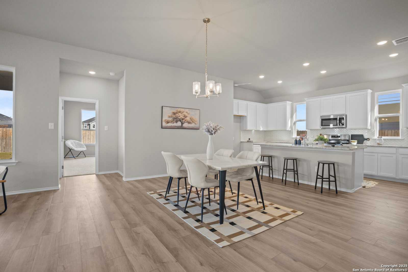 Open-concept dining area with white table, chairs, and patterned rug beside white cabinet kitchen in Davidson Homes The Collin B, Seguin, Texas
