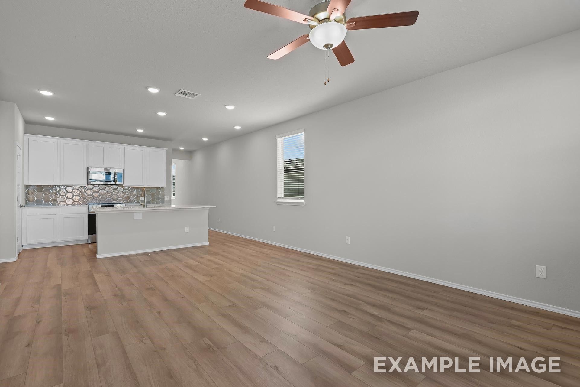 Open-concept living room and kitchen with wood-look flooring in Davidson Homes The Colorado G floor plan in Heartland, TX.