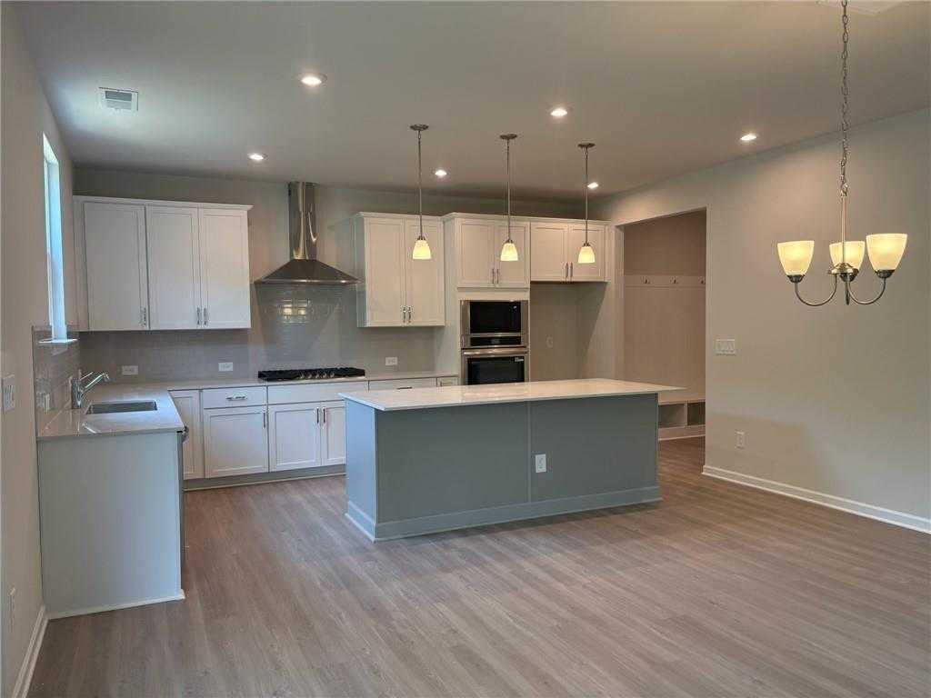 Modern white cabinet kitchen with gray island, stainless ovens, and pendant lights in Davidson Homes Hickory B, Riverwood, Dallas, GA