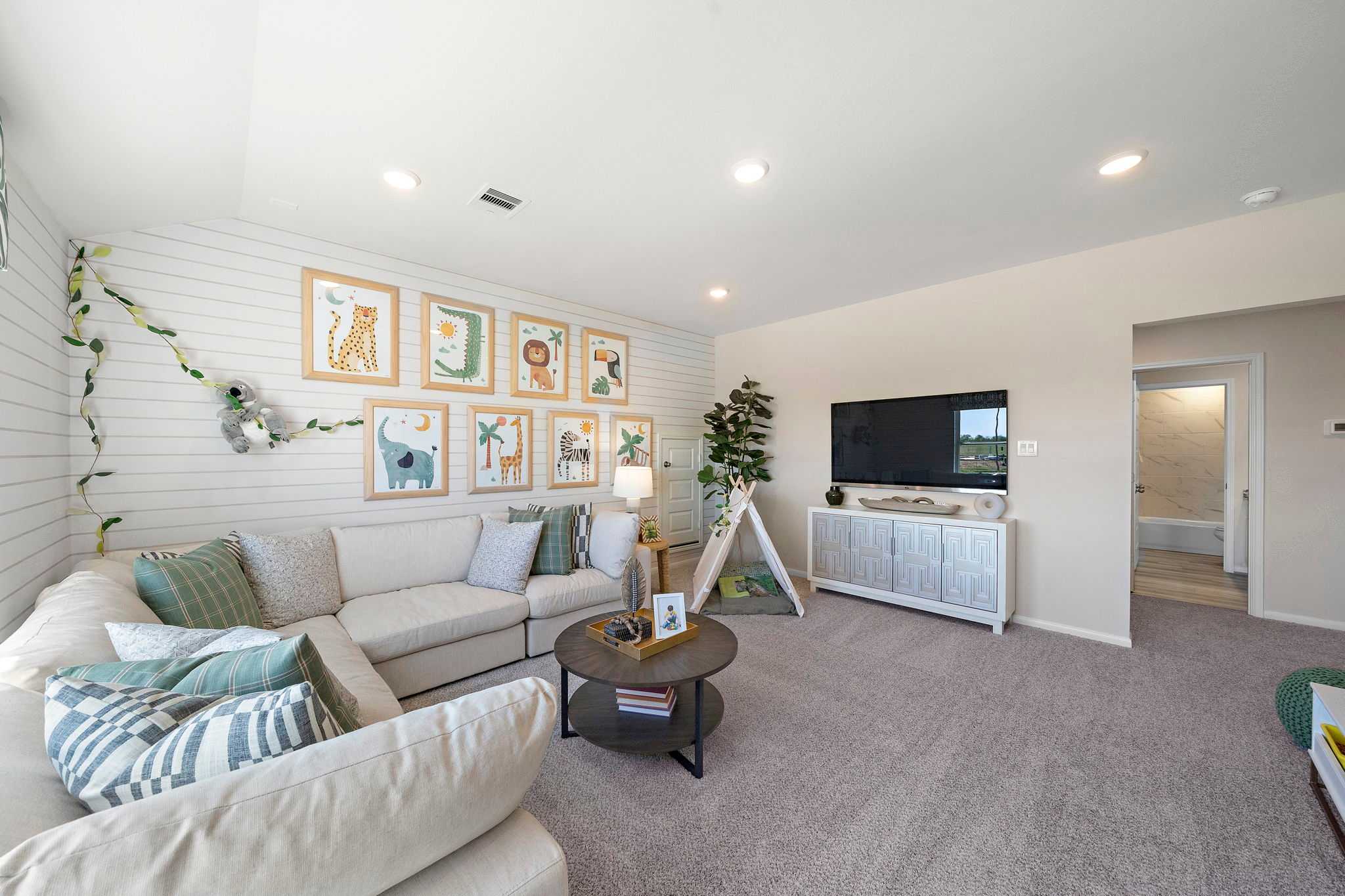 Cozy family room with shiplap walls, beige sectional sofa, animal art frames, and kids' tent at River Ranch Meadows in Dayton, Texas