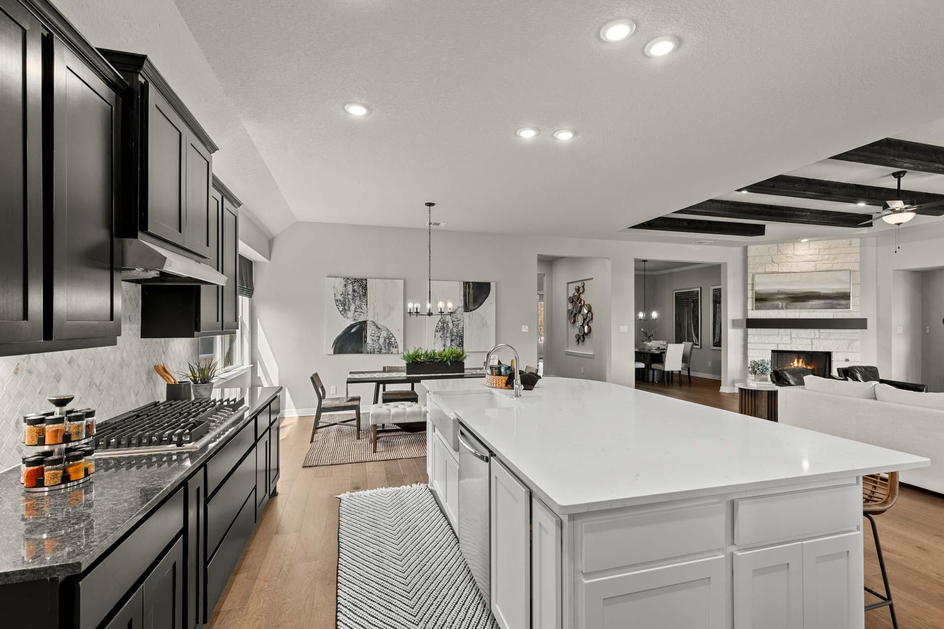 Spacious open-concept kitchen at Potranco Oaks in Castroville Texas with black cabinets white quartz island bar stools and adjacent living area