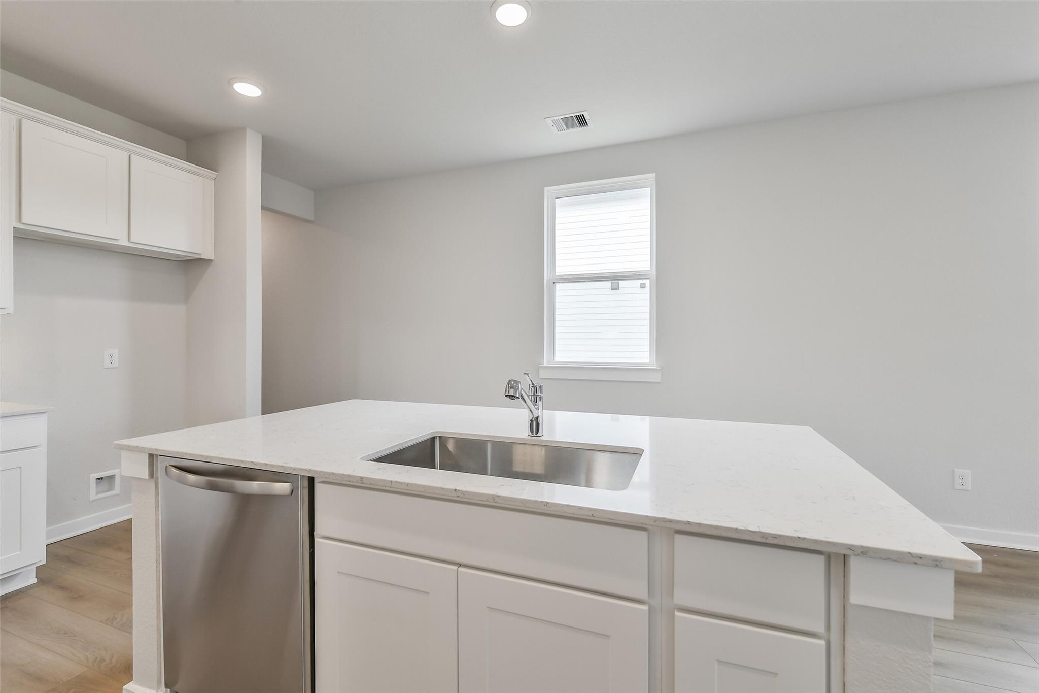 Modern kitchen with white cabinetry, quartz island sink, stainless dishwasher in Davidson Homes The Frio G, Cleveland, TX