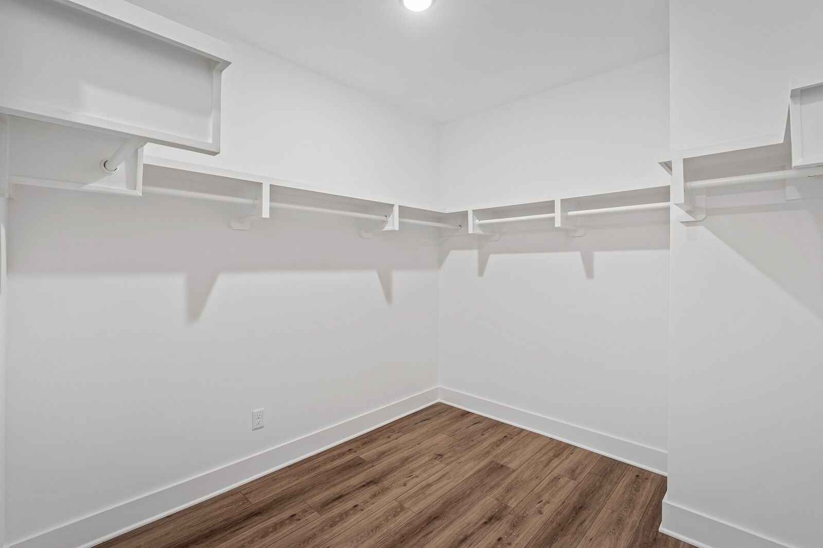 Spacious white walk-in closet with built-in shelving and hanging rods on hardwood floors in The Hawkins floor plan, Davidson Homes, Murfreesboro, TN
