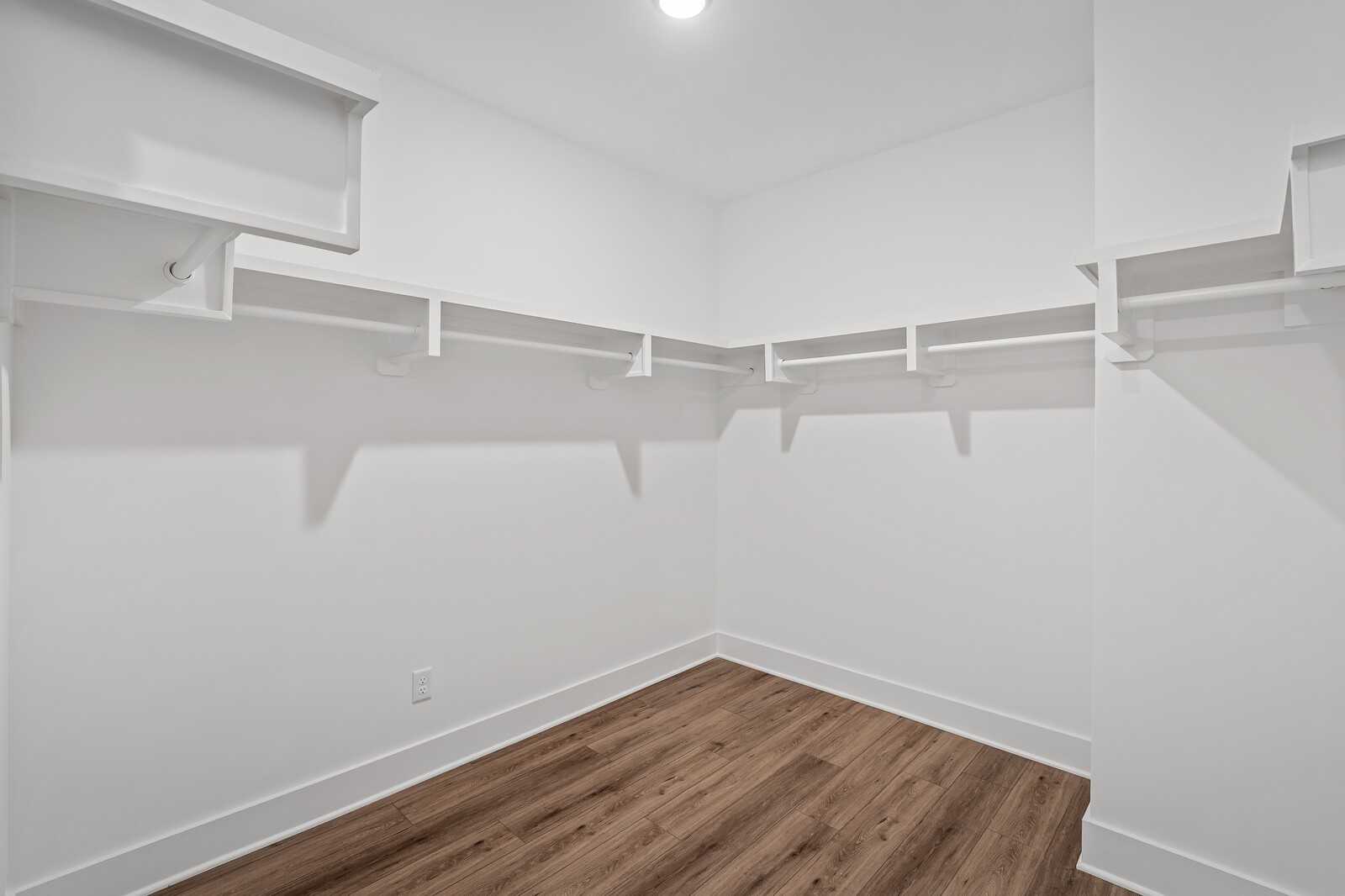 Spacious white walk-in closet with built-in shelving and hanging rods on hardwood floors in The Hawkins floor plan, Davidson Homes, Murfreesboro, TN