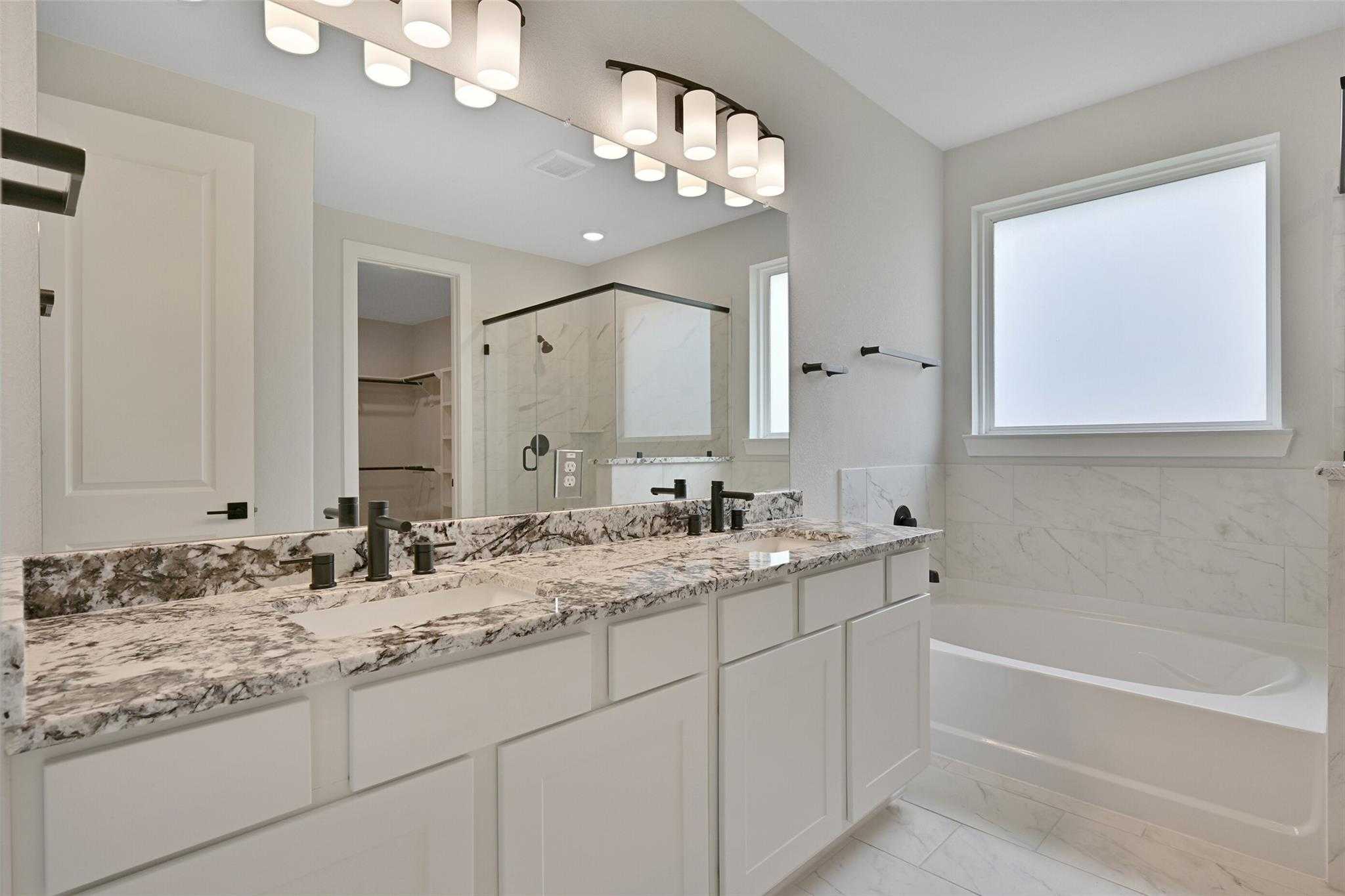 Elegant master bathroom with double granite vanity, modern faucets, soaking tub, and glass shower in Davidson Homes The Edward C, Lago Mar, Texas City