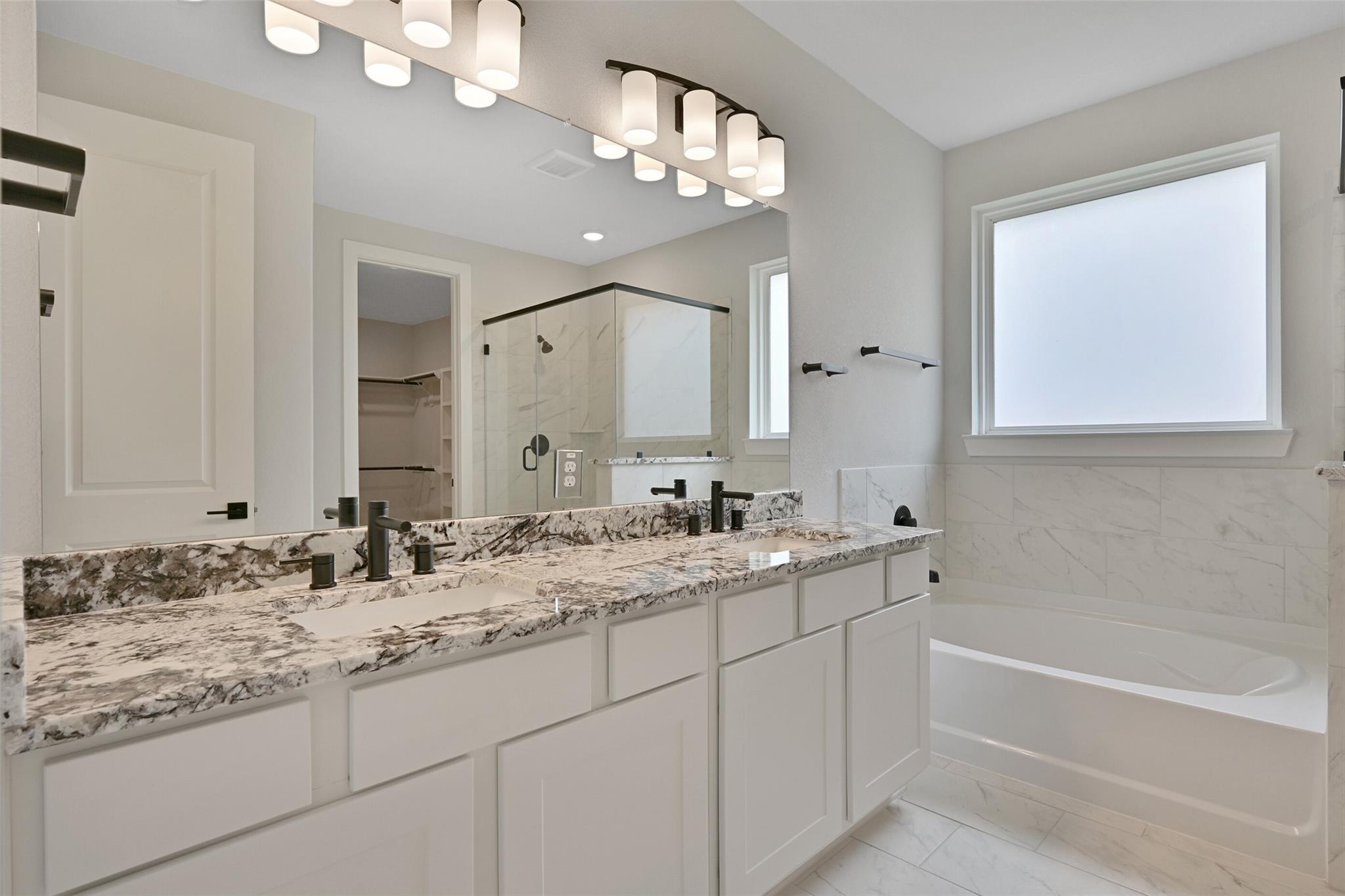 Elegant master bathroom with double granite vanity, modern faucets, soaking tub, and glass shower in Davidson Homes The Edward C, Lago Mar, Texas City