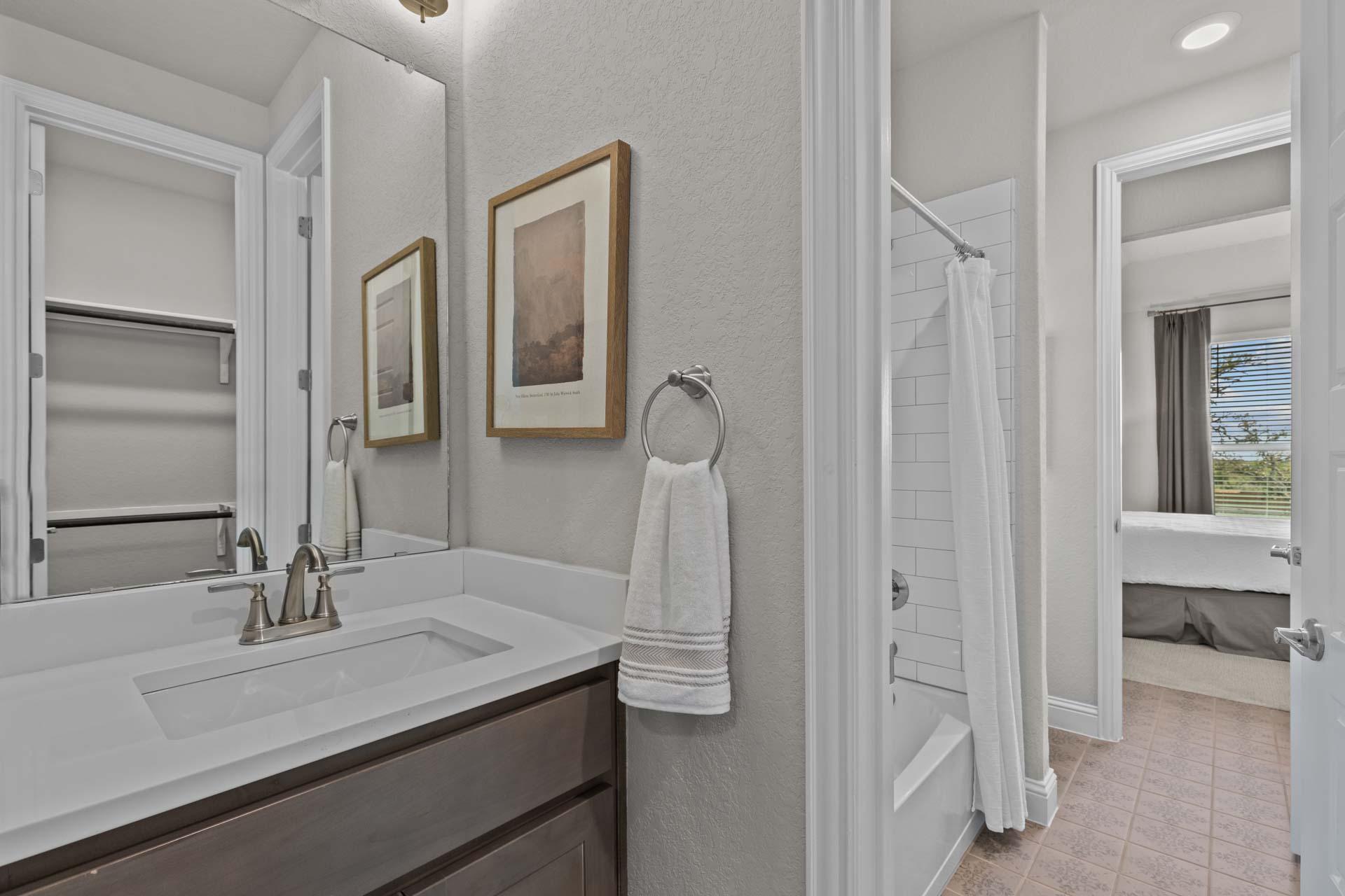The Garner A master bathroom featuring modern vanity, framed art, towel rack, walk-in shower, and bedroom view