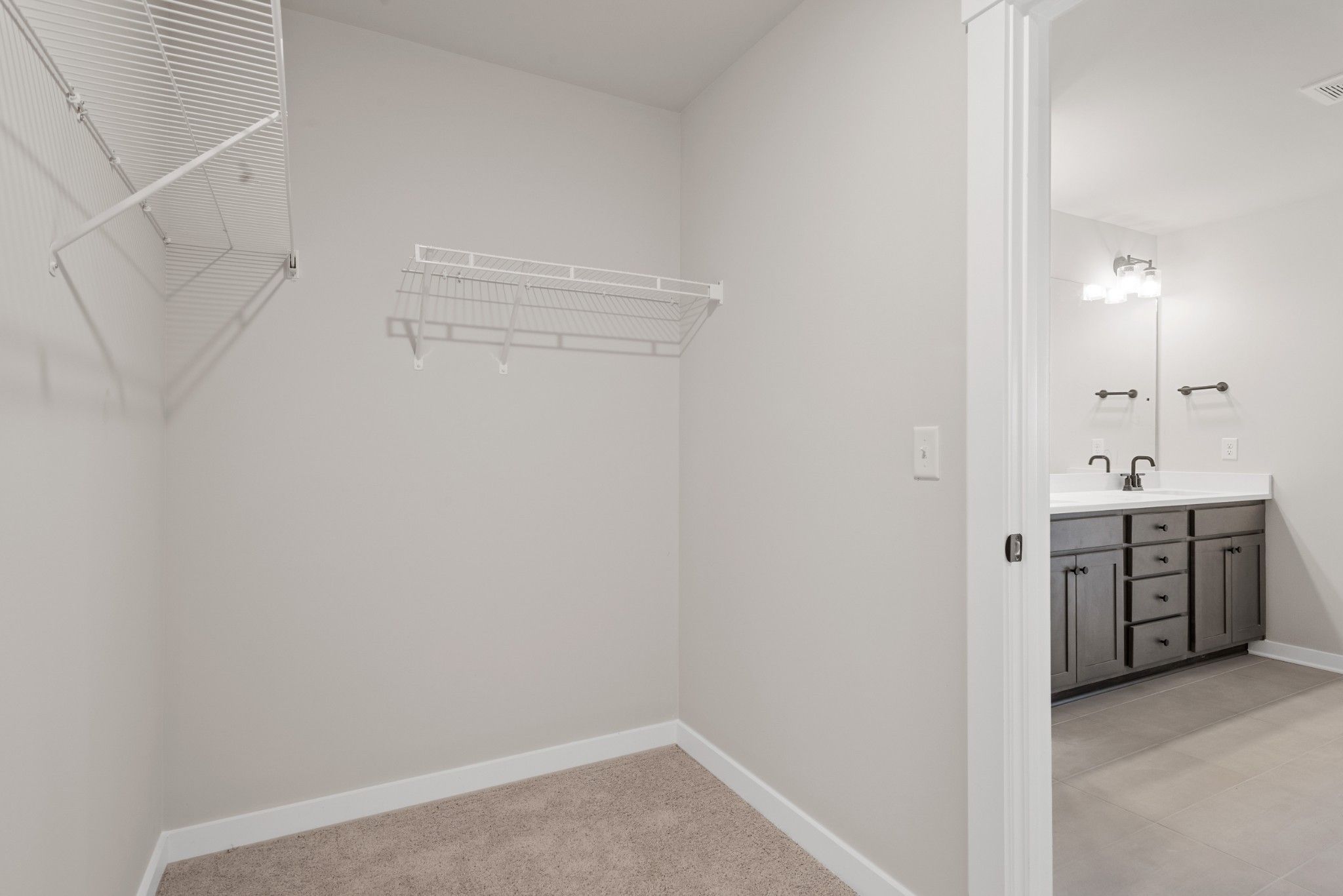 Spacious walk-in master closet with wire shelving beside en-suite bathroom double vanity in Davidson Homes The Willow B, White House, TN