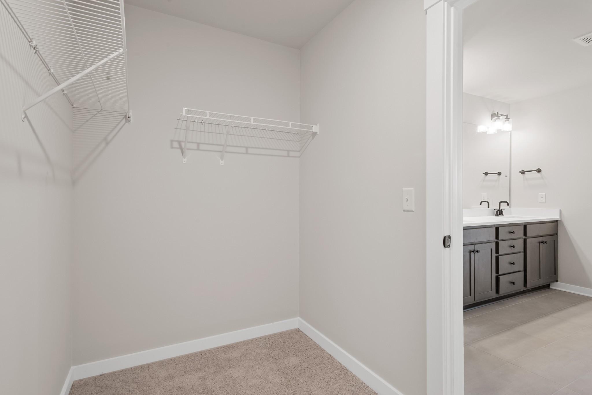 Spacious walk-in master closet with wire shelving beside en-suite bathroom double vanity in Davidson Homes The Willow B, White House, TN