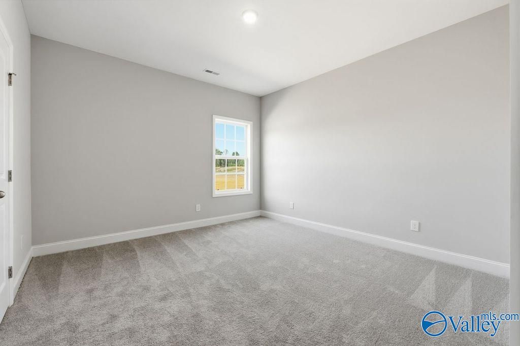 Spacious empty bedroom with light gray walls, gray carpet, large window to fields in Davidson Homes The Harrison, Hartselle, Alabama