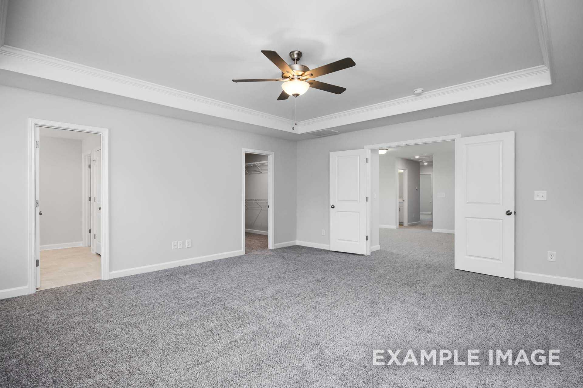 Spacious master bedroom in The Preston B featuring gray carpet, ceiling fan, and open doorways to bath and closet