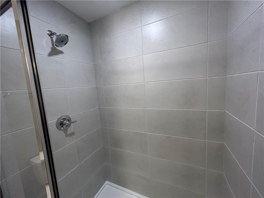 Modern glass-enclosed shower with chrome fixtures and light gray tile walls in Davidson Homes The Washington bathroom, Phenix City, Alabama