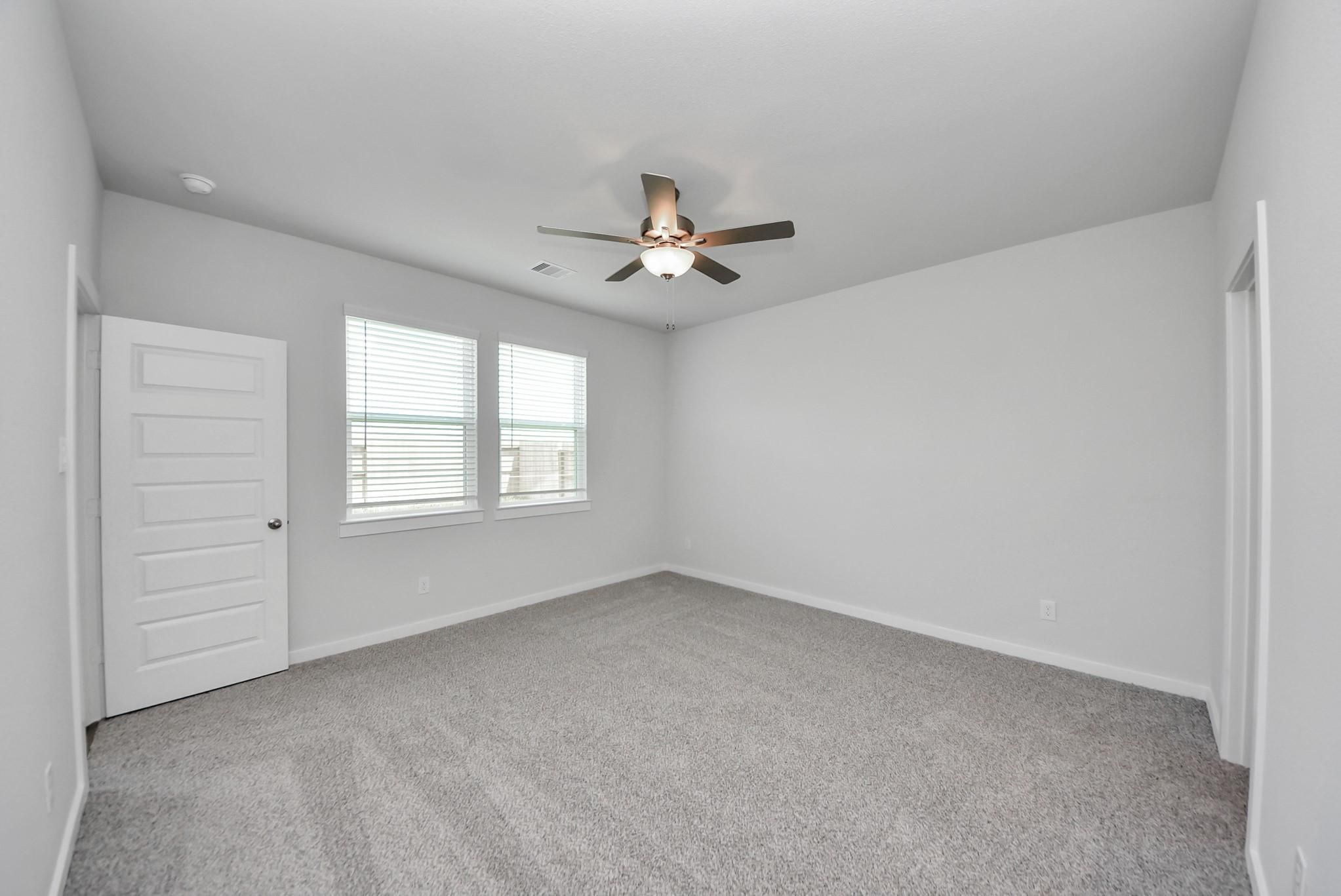 Spacious carpeted bedroom with ceiling fan and dual windows in Davidson Homes The San Marcos E, Emberly, Beasley, Texas