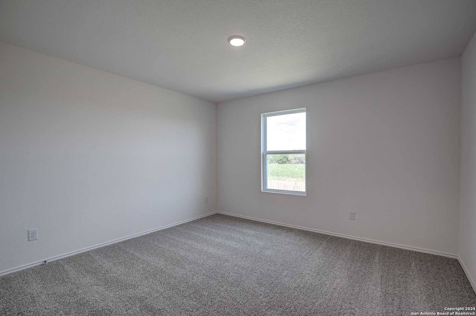 Bright empty bedroom with white walls, gray carpet, and large window in Davidson Homes The Douglas D, Seguin, Texas