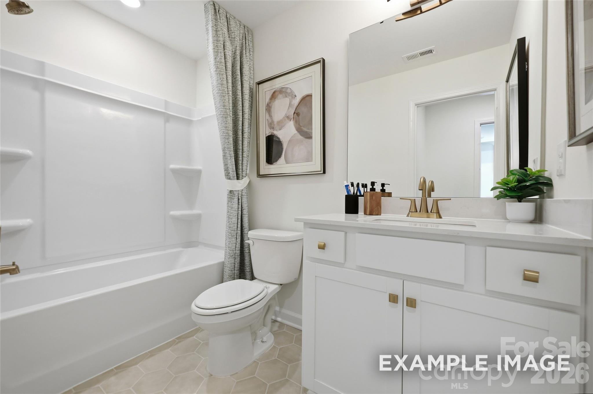 Bright white bathroom with tub, toilet, and vanity with gold fixtures in Davidson Homes The Aspen B, Windgate, Mooresville, NC