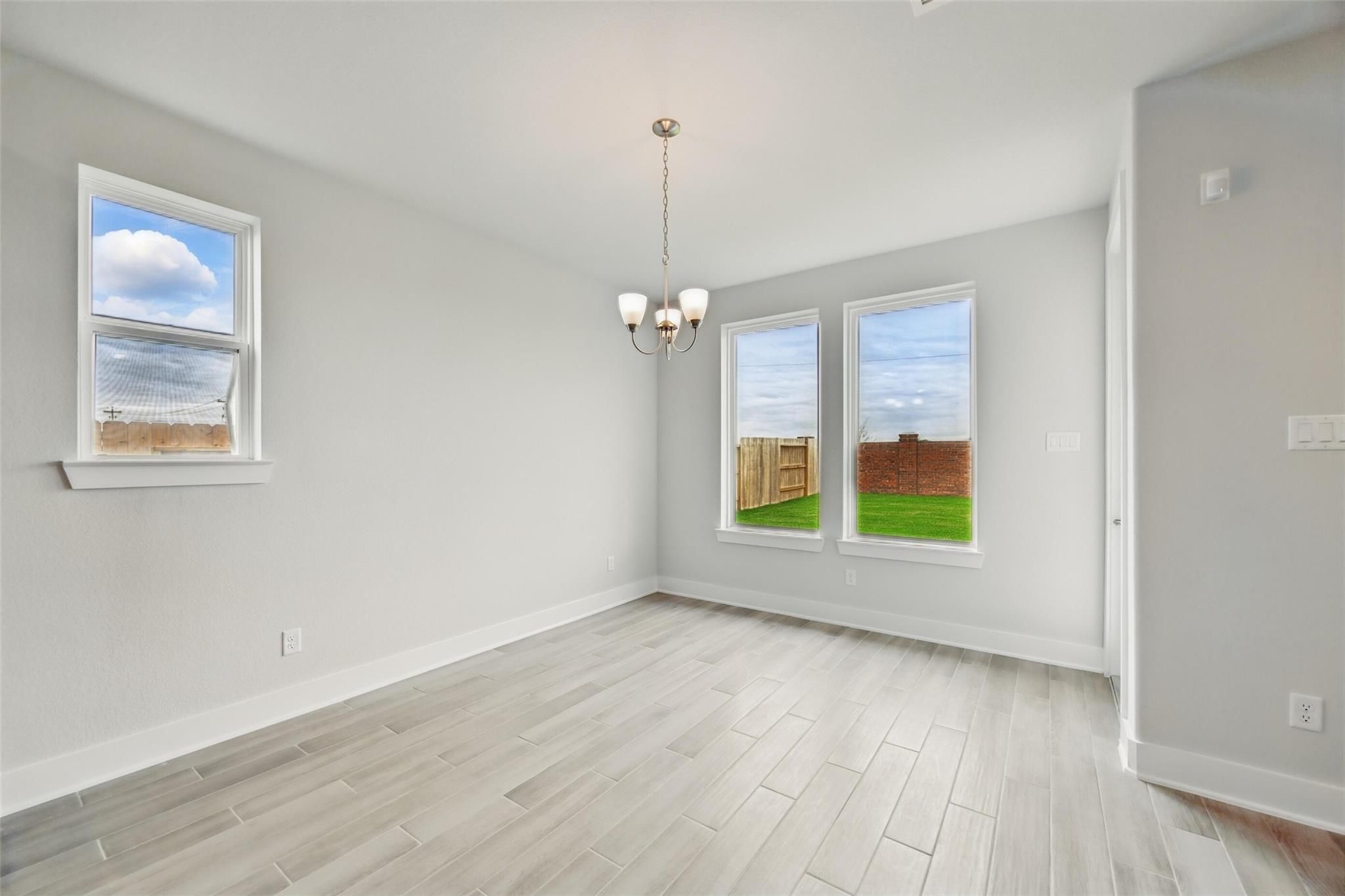 Bright dining room with chandelier, light wood floors, gray walls, and large windows overlooking fenced backyard in Davidson Homes The Philip A, Lago Mar, Texas City