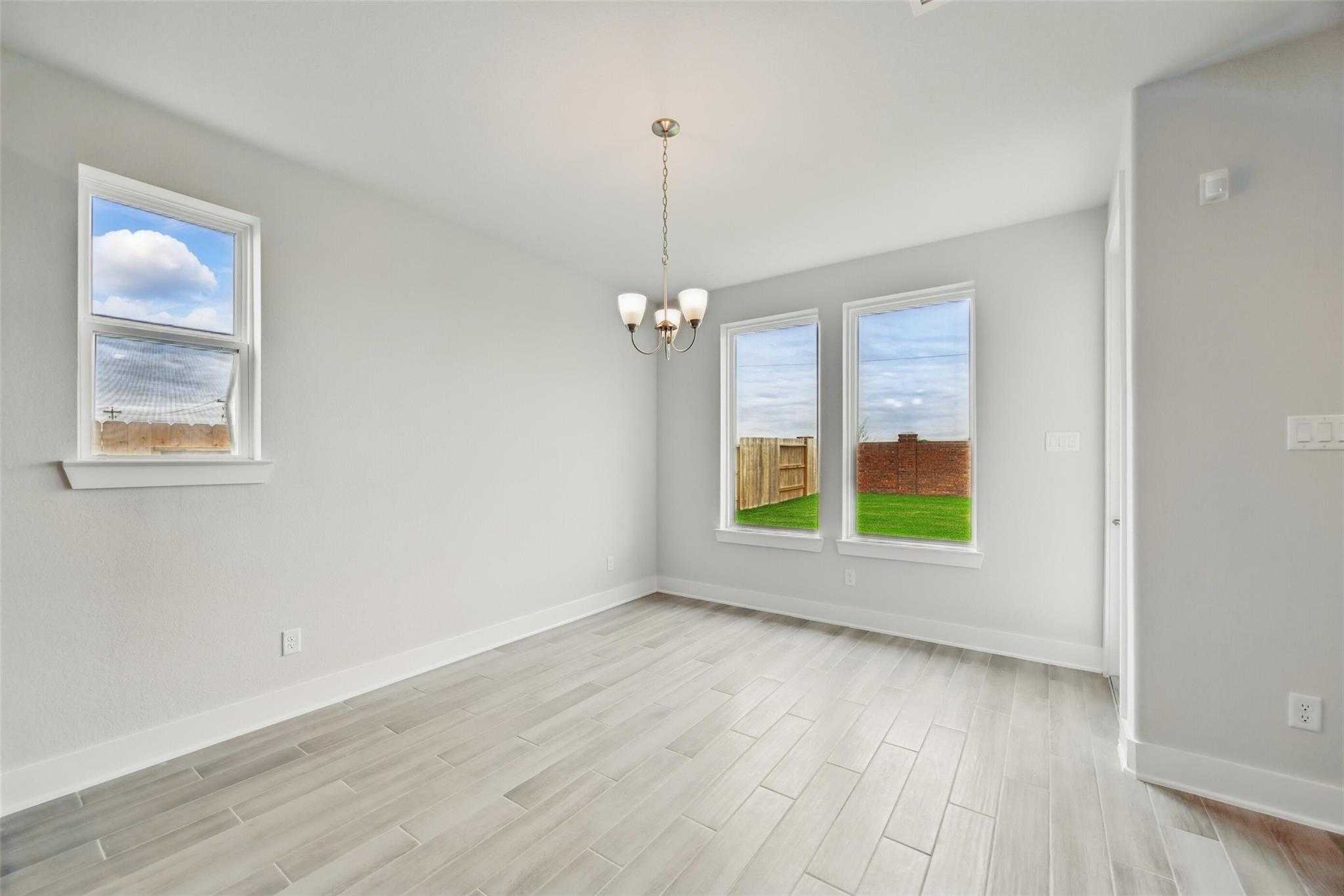 Bright living room with gray walls, hardwood floors, chandelier, and large windows overlooking green backyard in Davidson Homes The Philip A, Lago Mar, Texas City