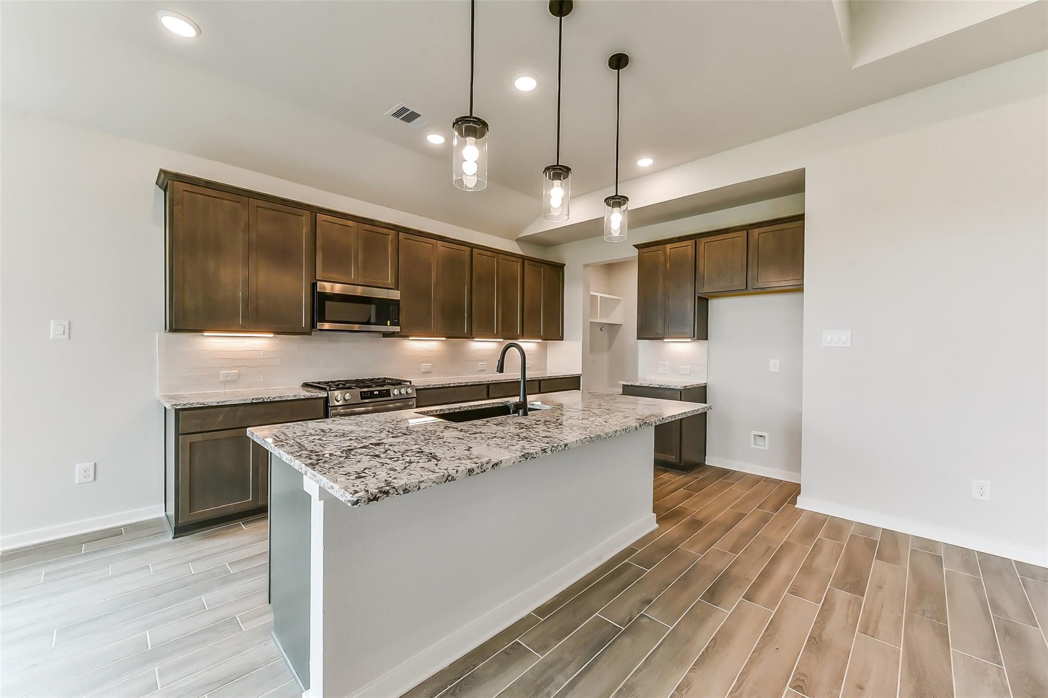 Modern kitchen with dark shaker cabinets, speckled granite island, stainless steel appliances, and pendant lights in The Sequoia C, Crosby, Texas
