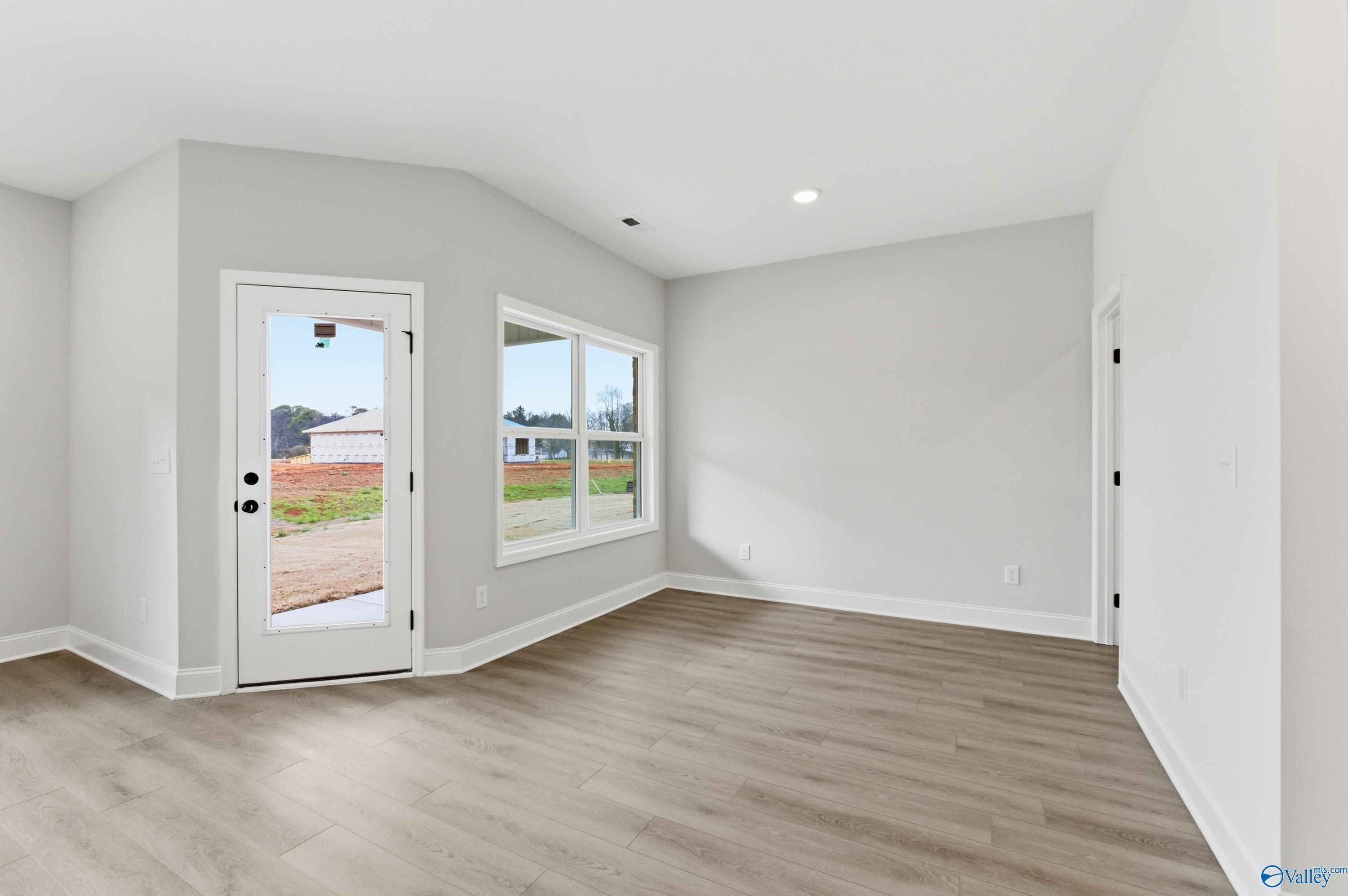 Bright empty living room with large windows overlooking green yard, light gray walls, hardwood floors in Davidson Homes The Daphne C, Huntsville AL