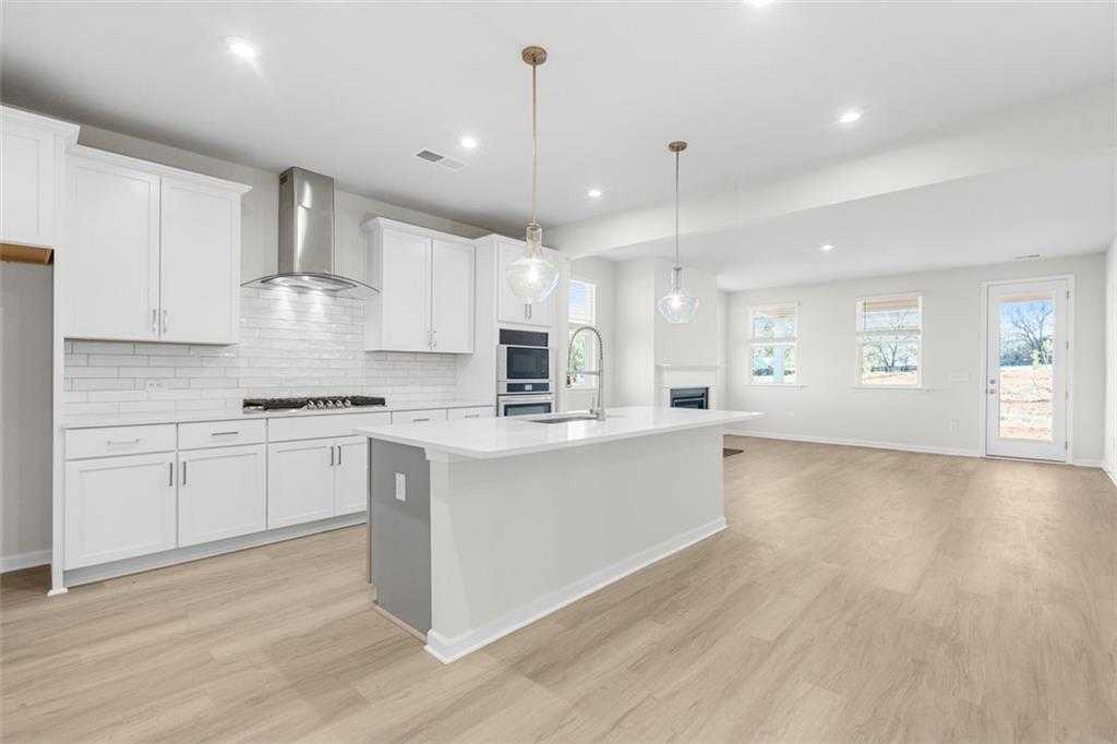 Modern white kitchen with stainless steel appliances, subway tile backsplash, and large quartz island in Davidson Homes The Glenwood C, Hoschton, GA