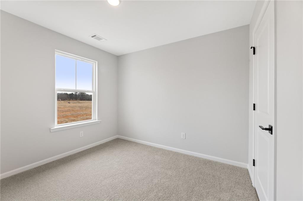 Bright secondary bedroom with gray walls, carpeted floor, and window view of rural fields in Davidson Homes The Rabun C, Winder, Georgia