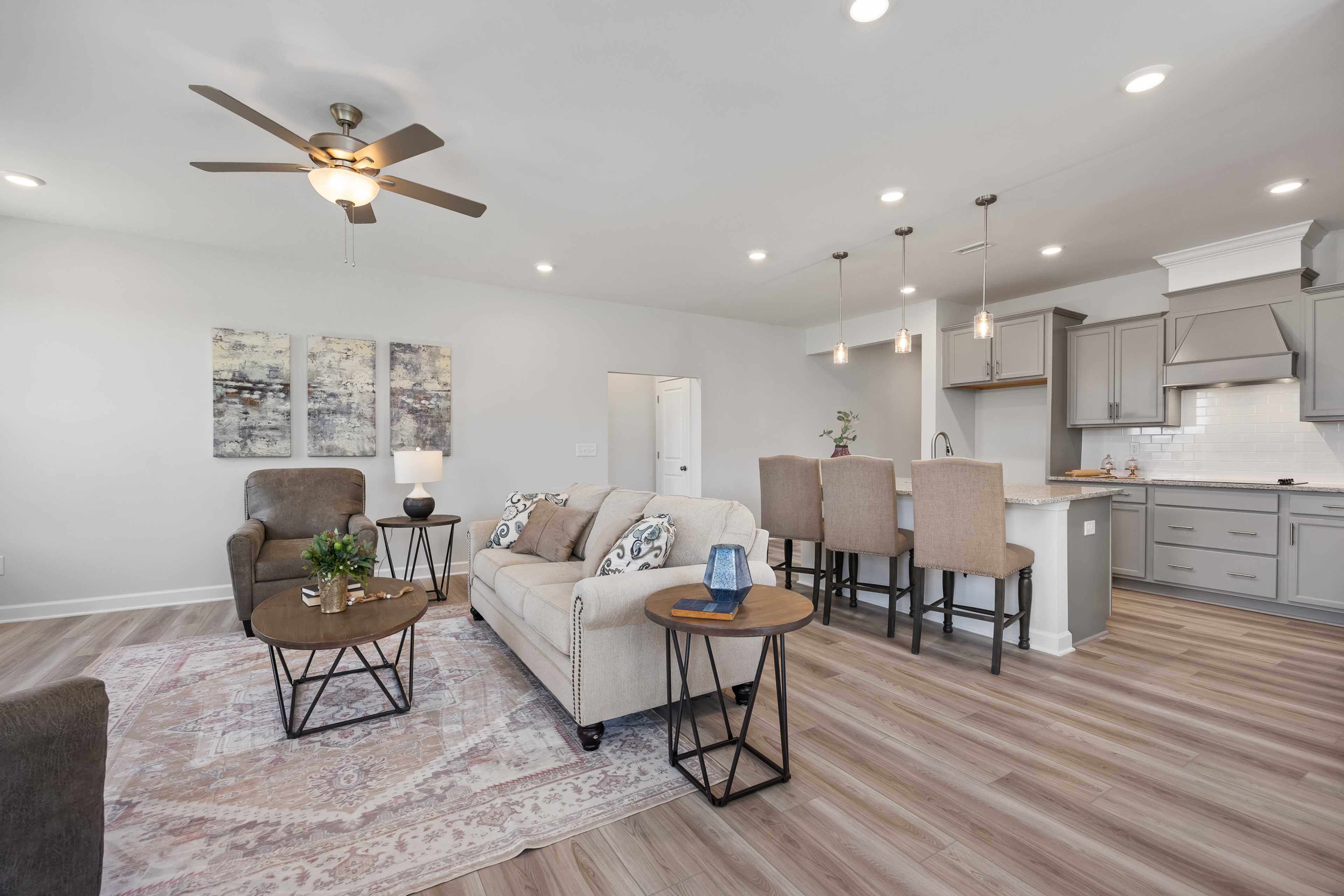 Open-concept living room and kitchen at Woodland Crossing in Zebulon NC with beige sofa, gray cabinets, hardwood floors, ceiling fan