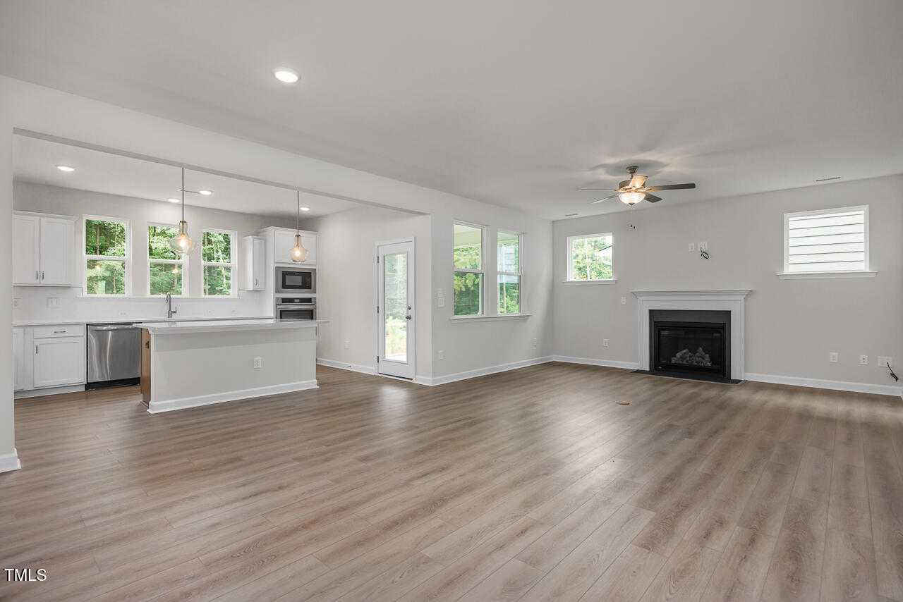 Open-concept kitchen with white cabinets and island adjacent to living room featuring fireplace and ceiling fans in Davidson Homes The Aspen B, Wake Forest, NC